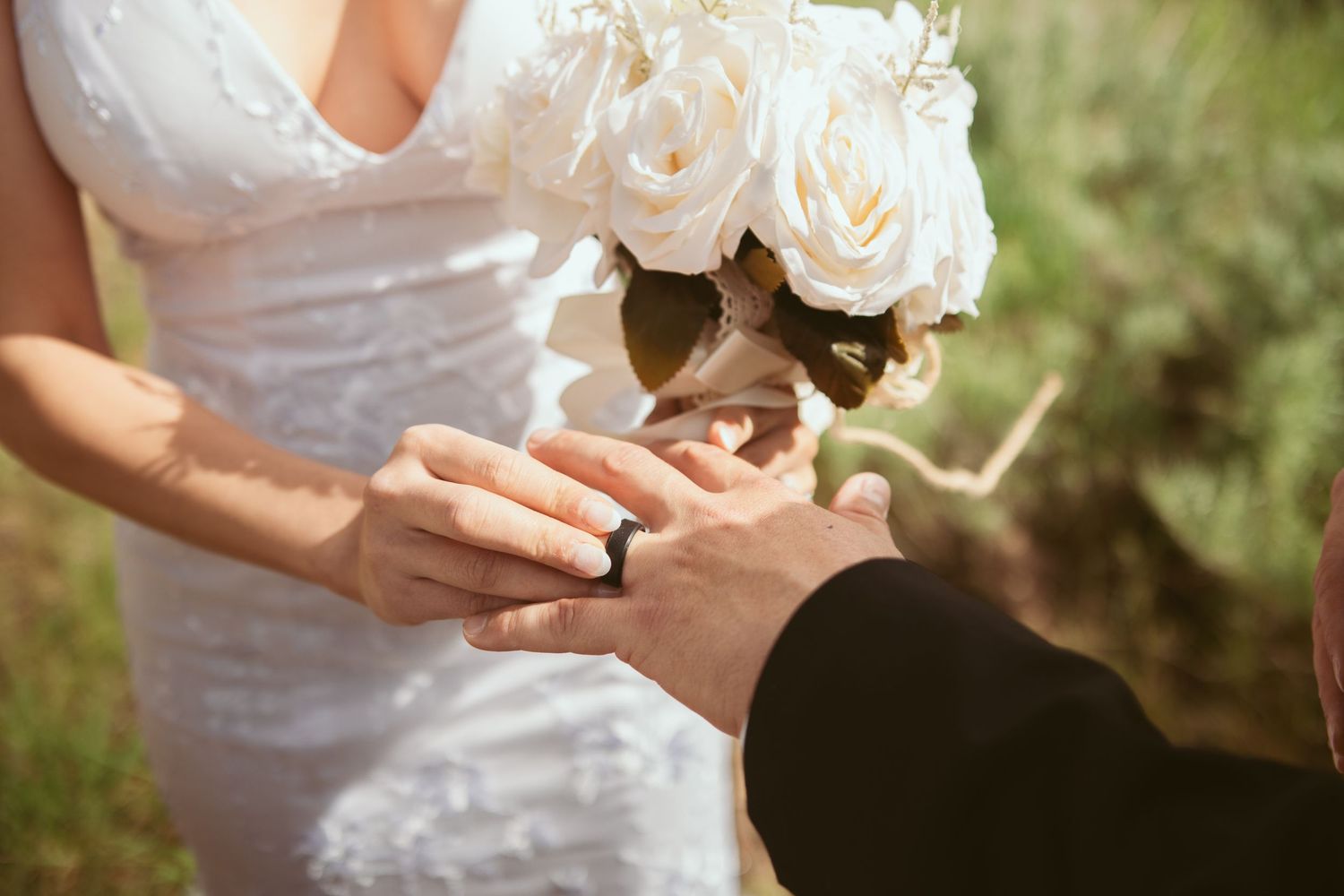A white rose wedding bouquet held against a natural outdoor backdrop.