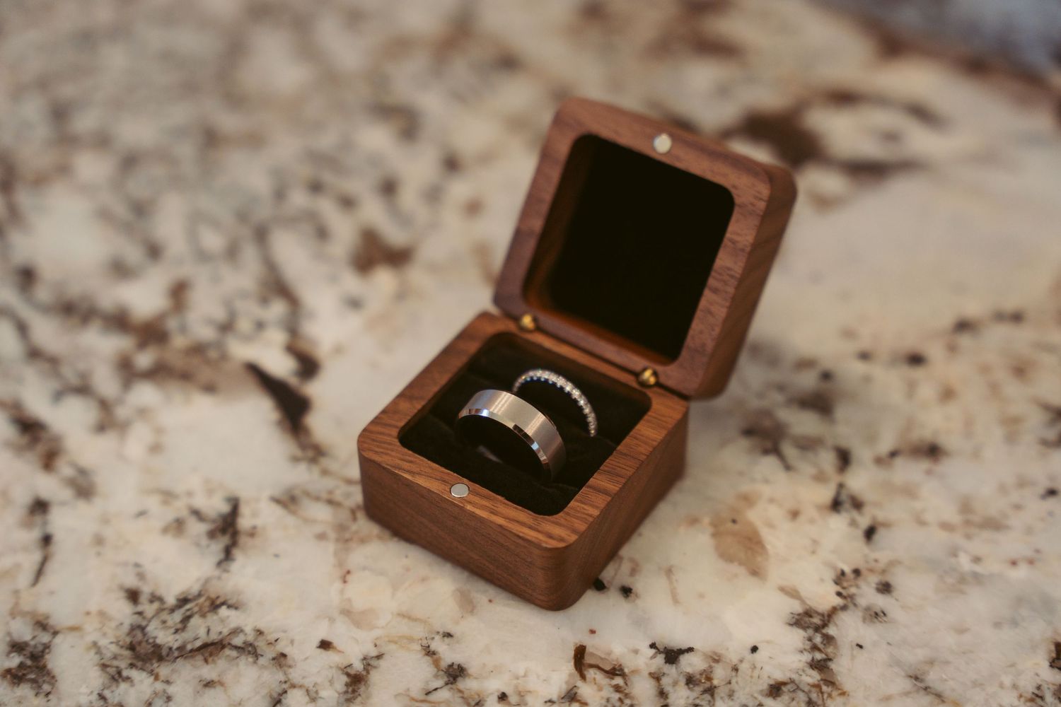 Wedding rings displayed in wooden boxes on marble countertop.