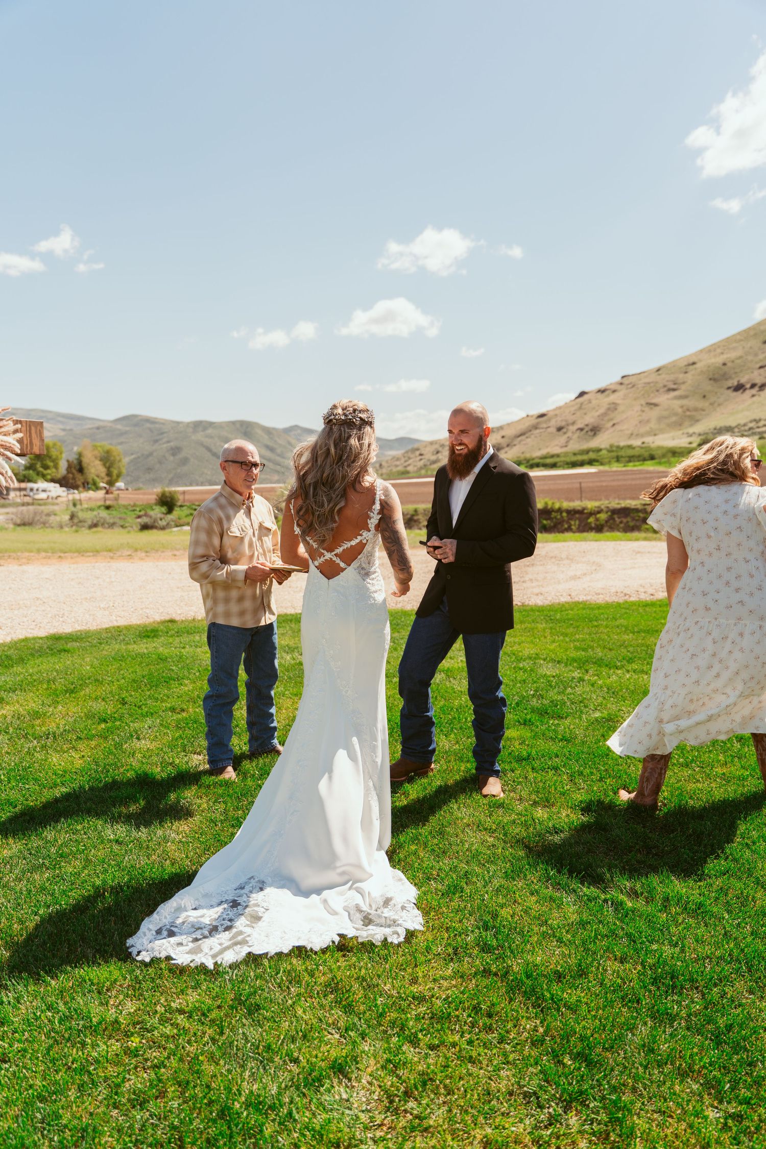 Wedding celebration on green lawn with wooden cross and mountain backdrop under blue sky.