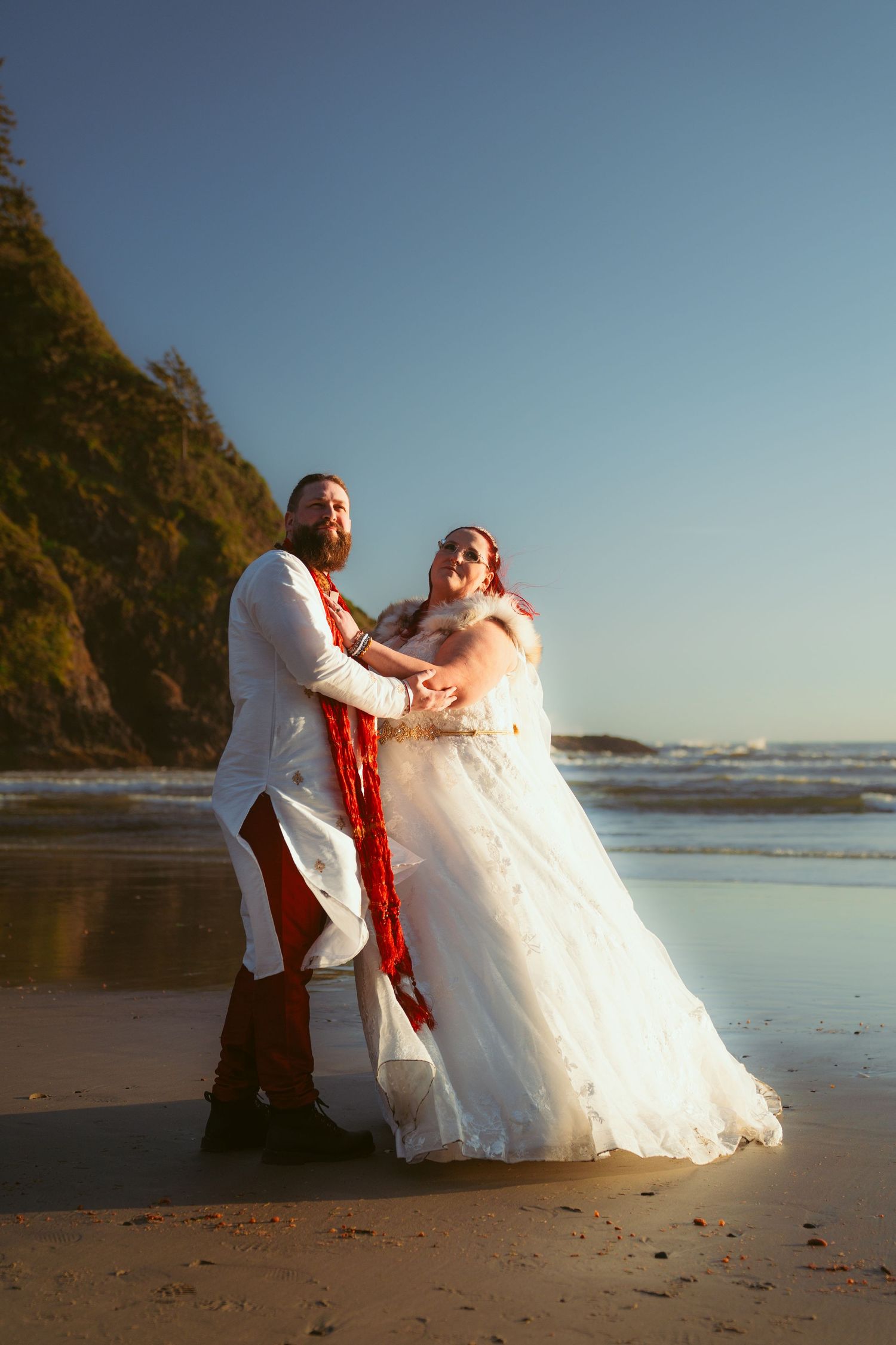 A couple dances joyfully on a reflective beach at golden hour.