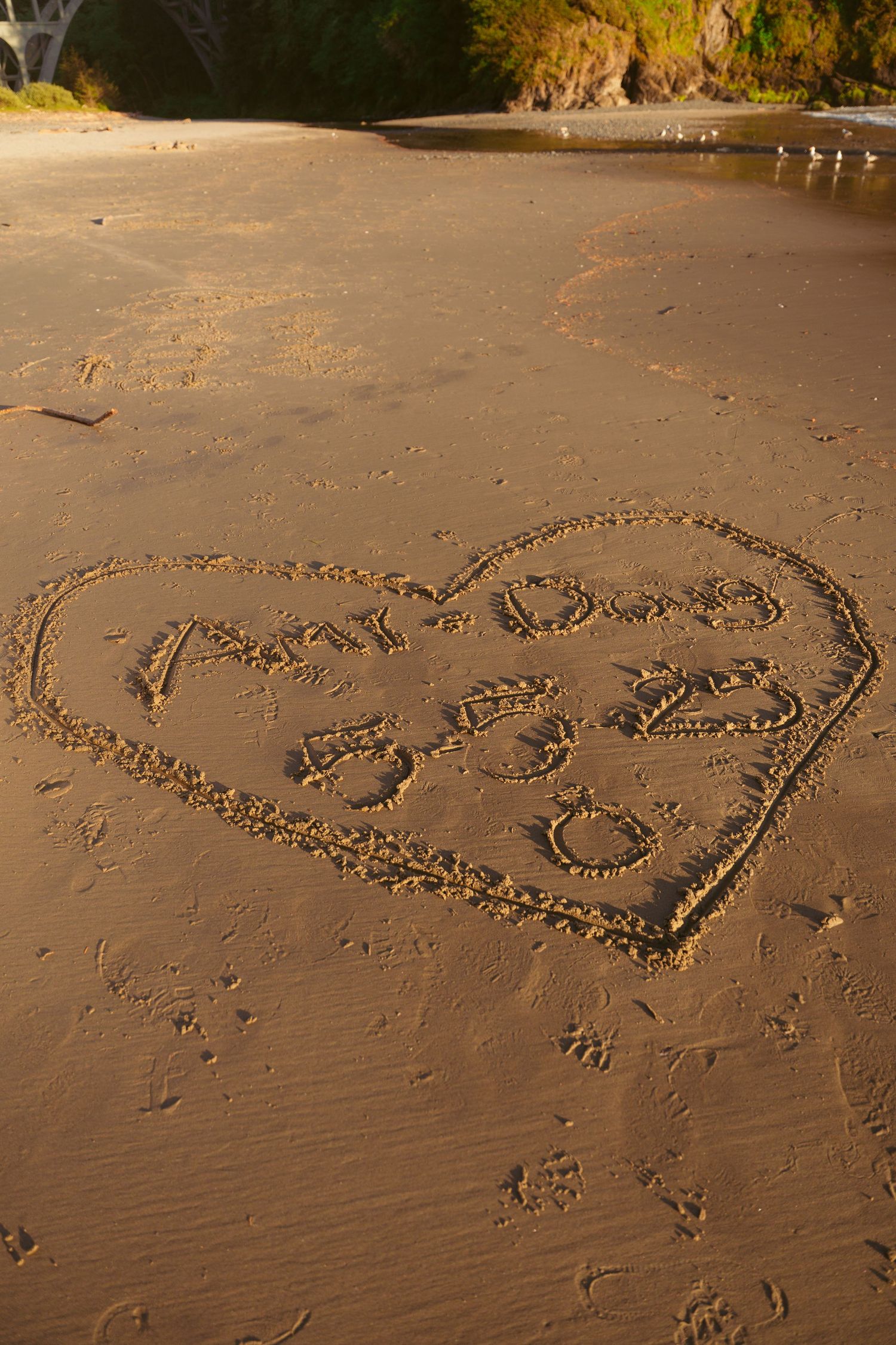 Heart shapes drawn in wet sand on a beach with footprints visible nearby.