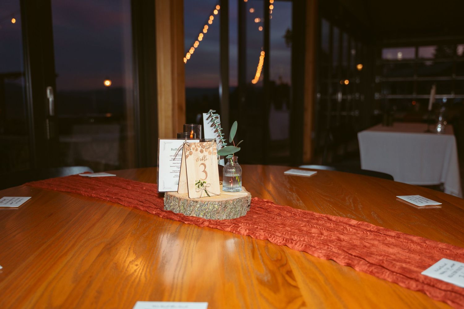 A small centerpiece with candles and decor on a wooden table with red table runner.