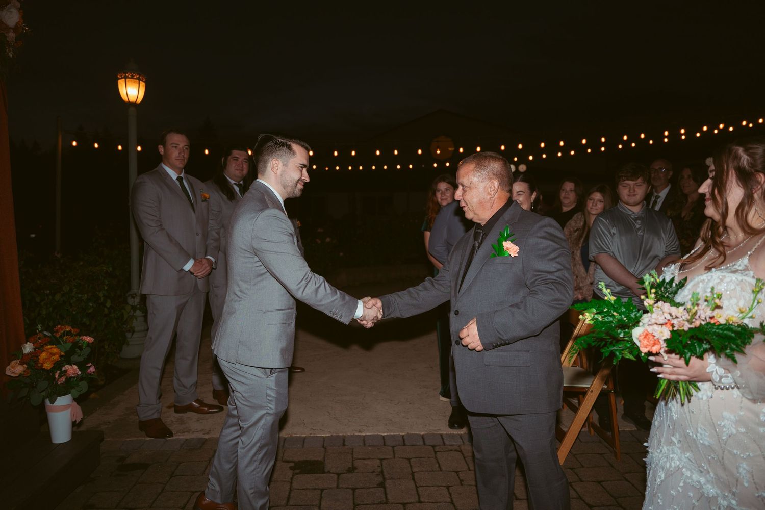 Couples dancing together during an evening wedding reception on a brick patio.