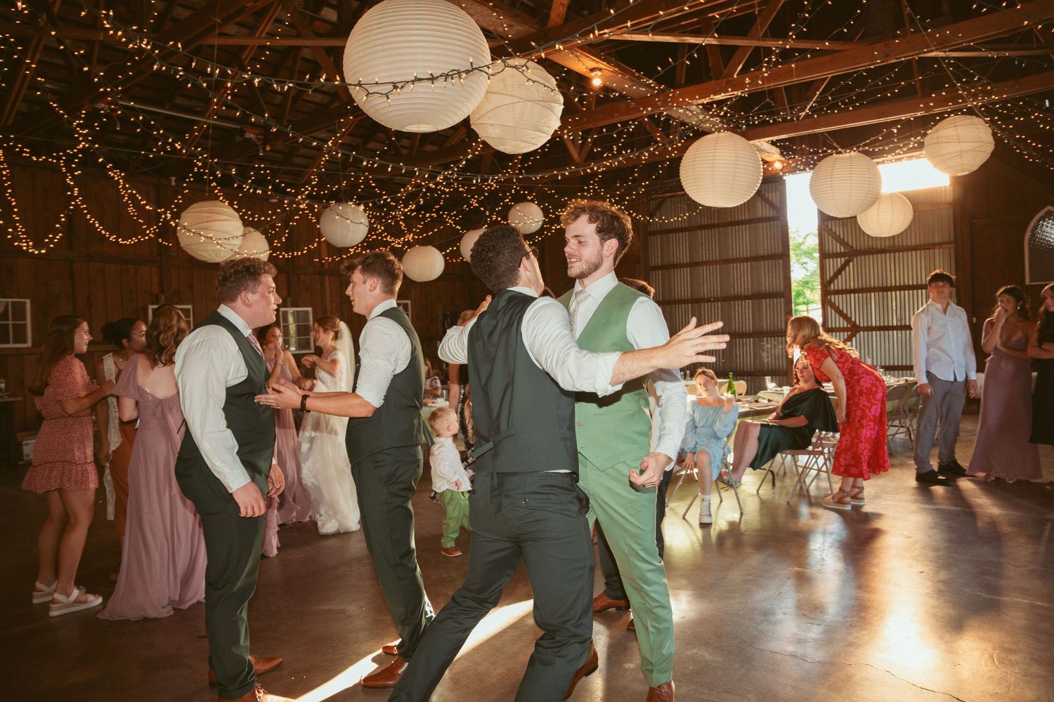 Wedding guests enjoying themselves on a dance floor illuminated by string lights and paper lanterns.