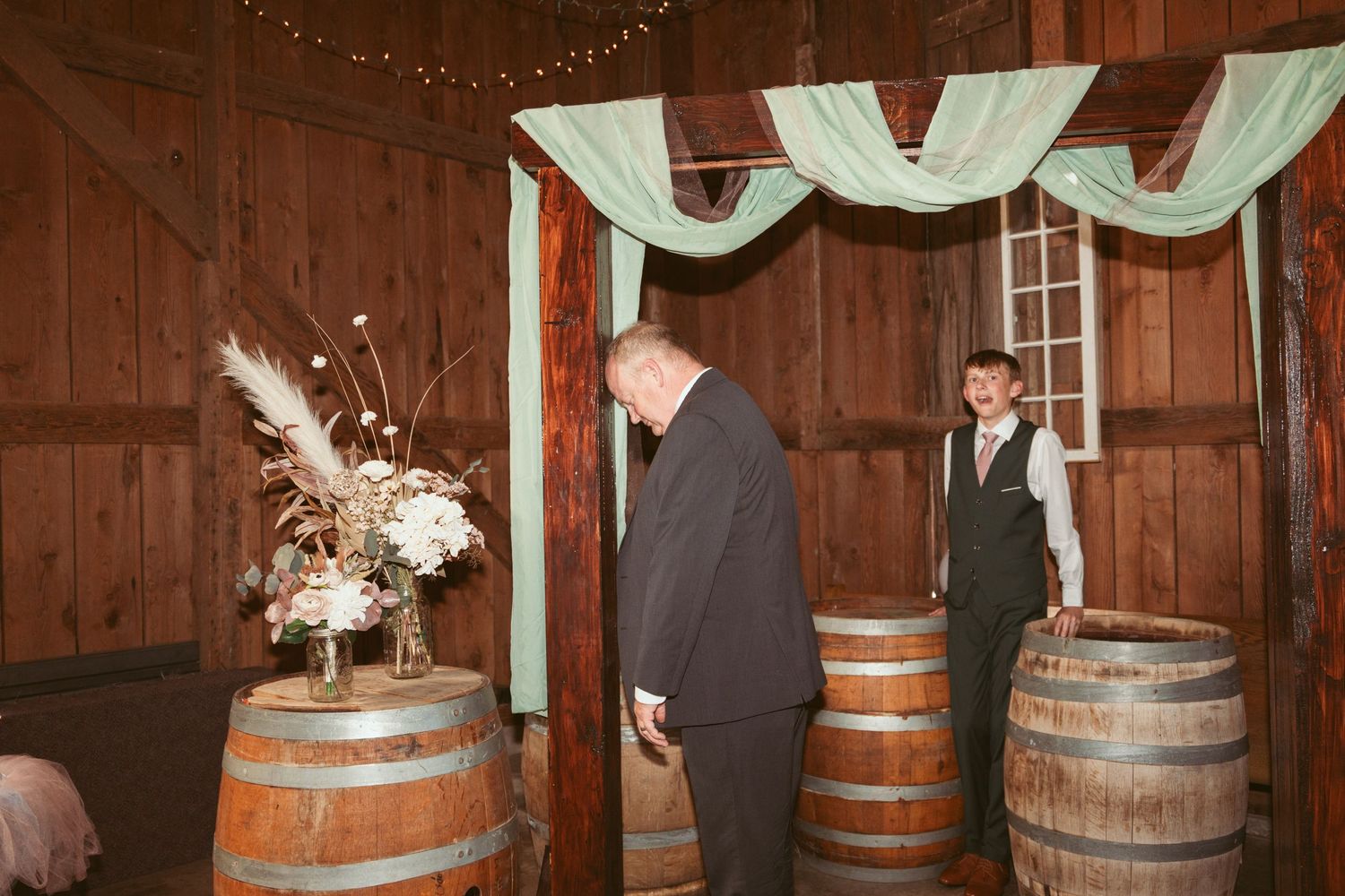 Rustic barn wedding decor featuring wooden barrels and elegant white fabric draping.