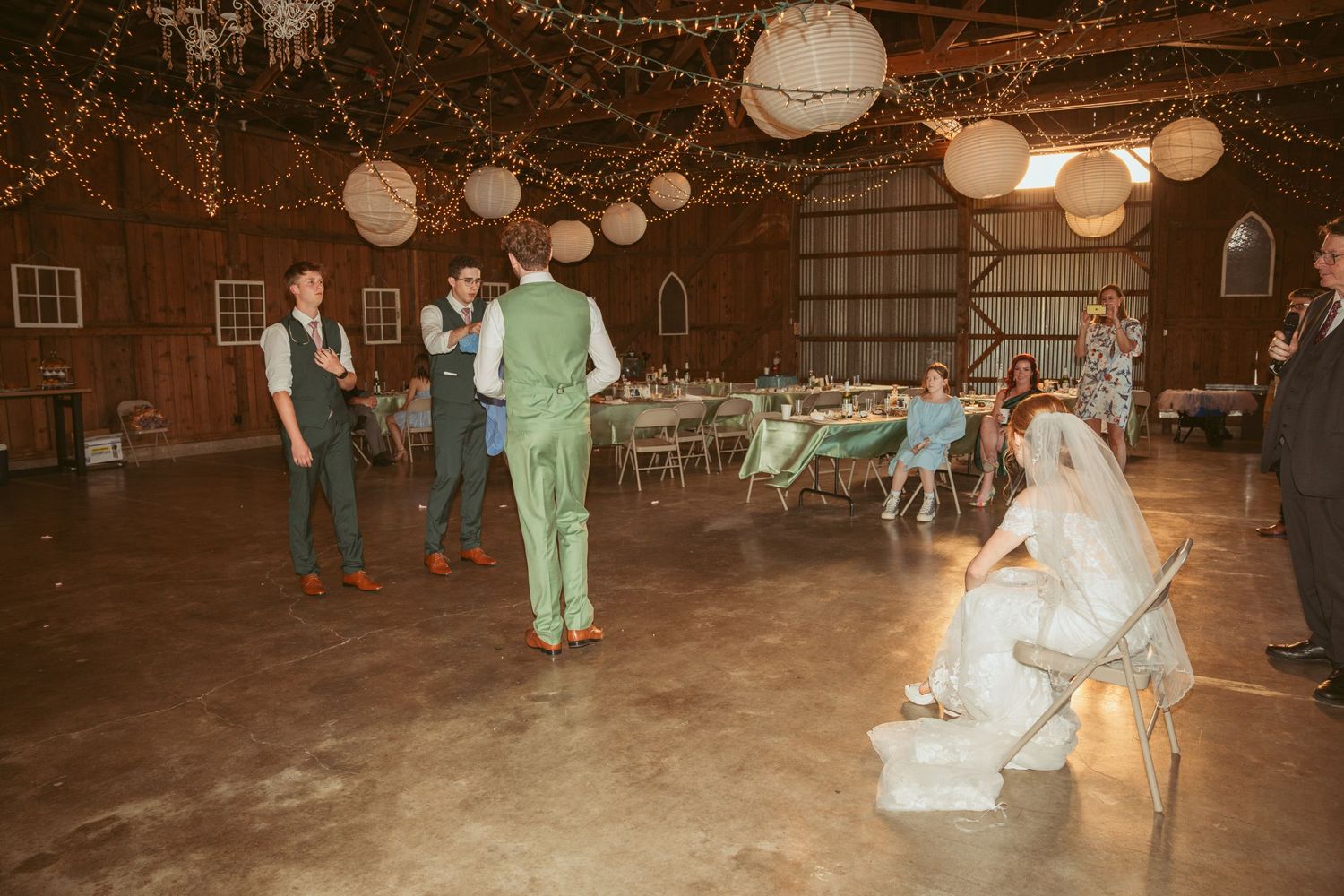 Wedding celebration in a barn with string lights overhead and guests dancing on the wooden floor.