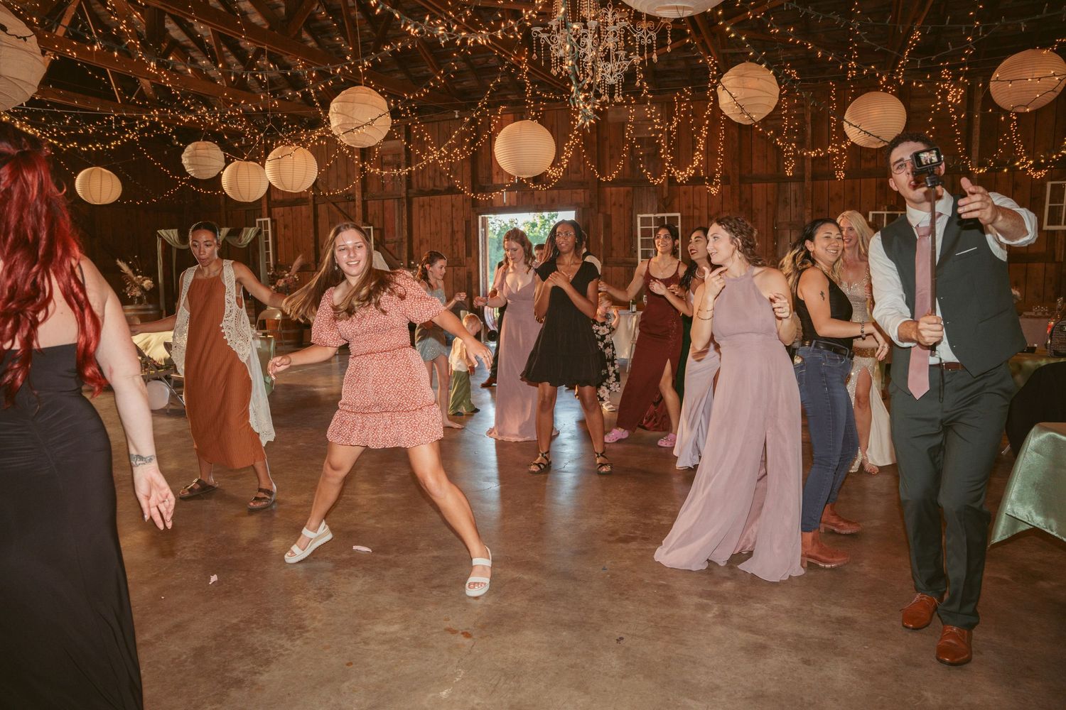 Wedding celebration with people dancing energetically under string lights and paper lanterns.