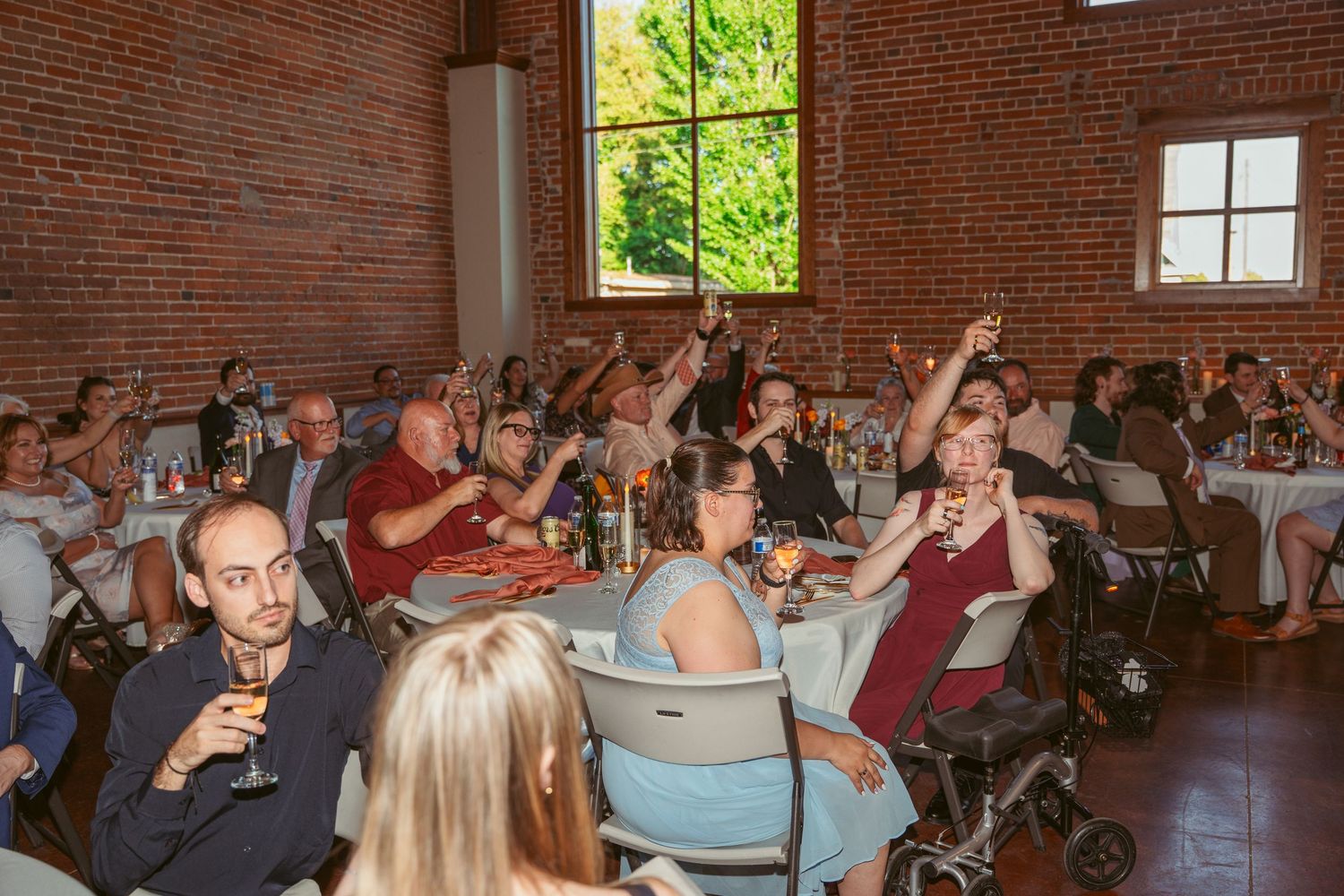Reception guests raising their glasses in celebration inside a rustic brick venue.