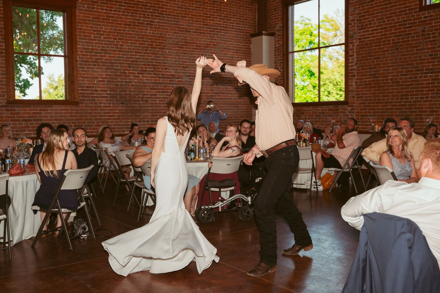 Wedding celebration features dynamic dance moves in a rustic venue with exposed brick walls.
