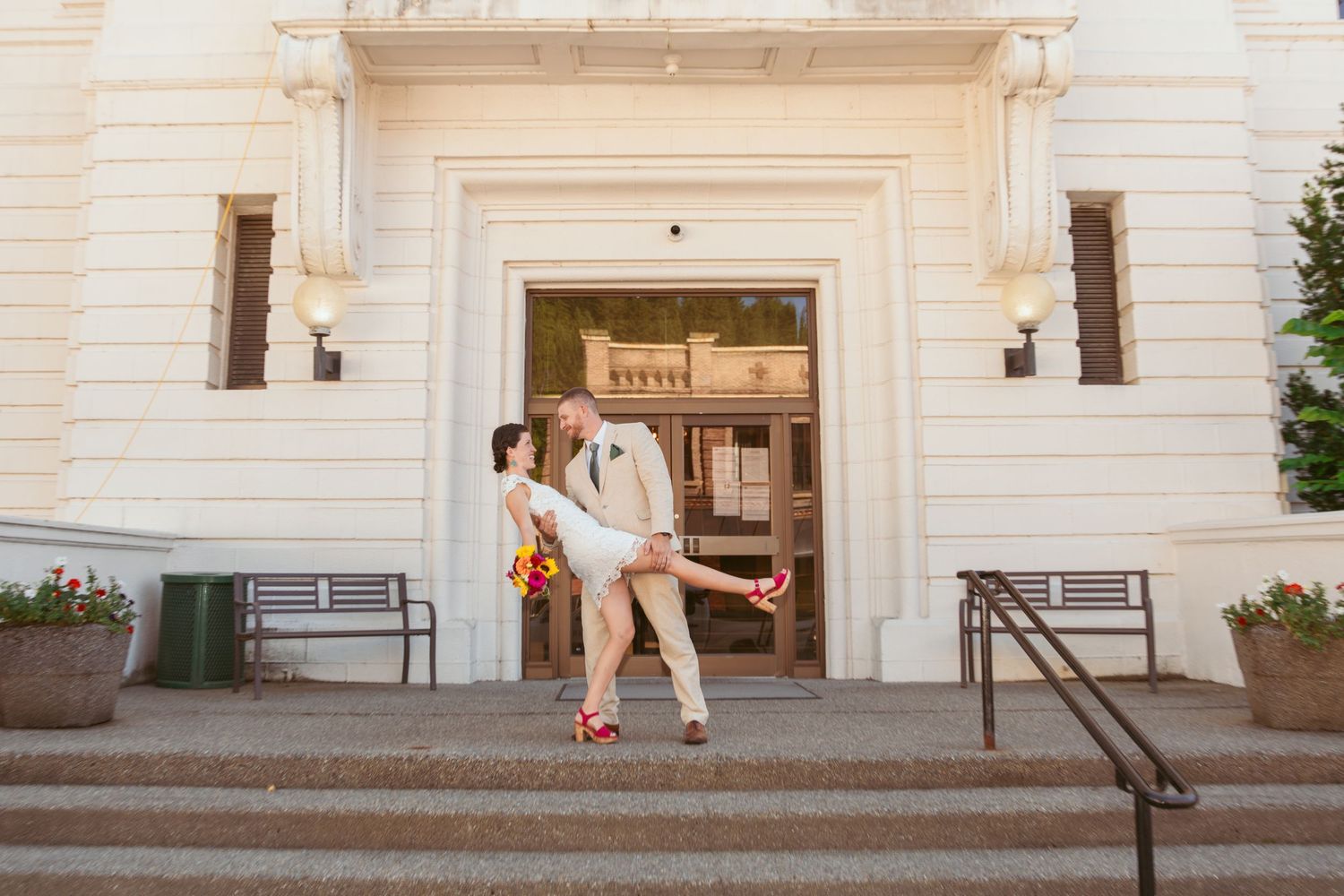 A couple shares a tender moment on stone steps outside a white building.
