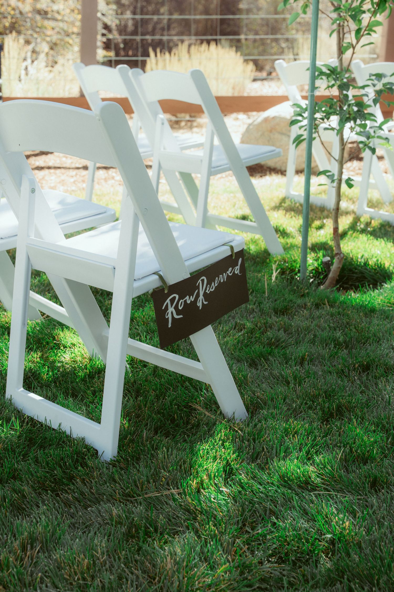 White wooden folding chairs arranged on grass for an outdoor ceremony.
