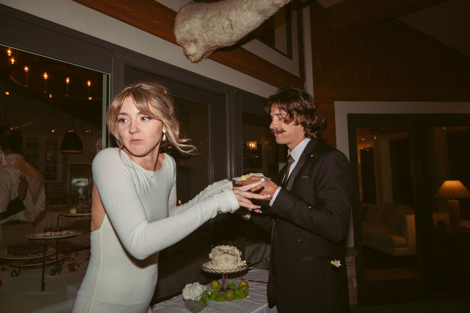 A couple enjoys a lighthearted cake feeding moment at their wedding reception.