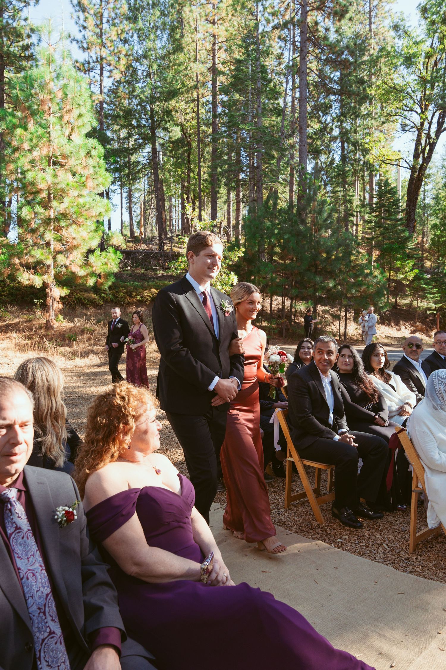 Wedding guests seated on wooden chairs during an outdoor forest ceremony.