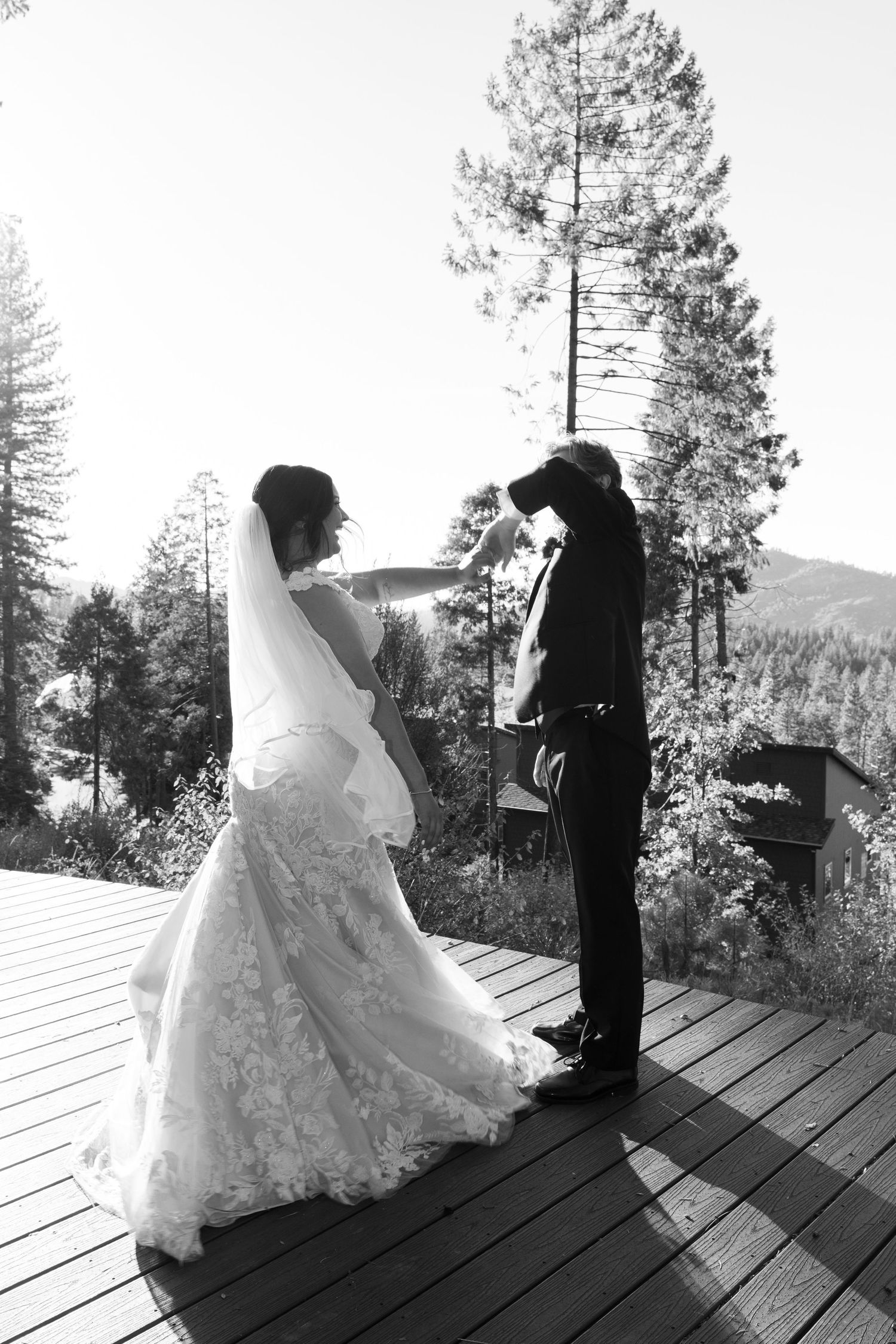 A wedding couple stands on a wooden deck overlooking mountain scenery in black and white.