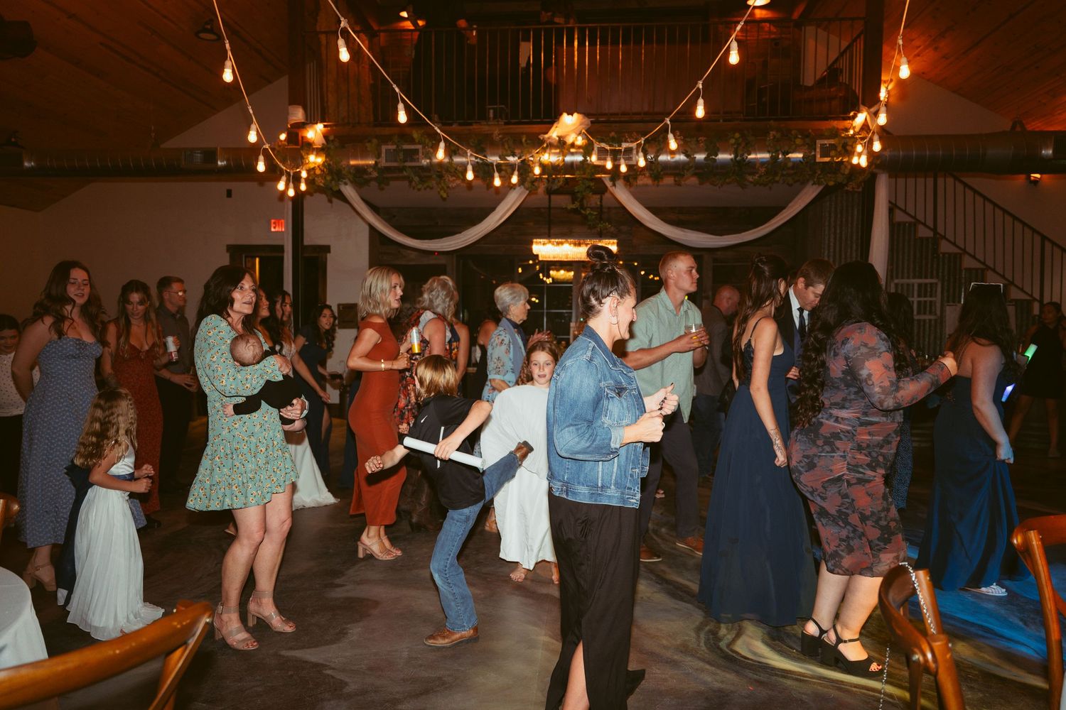 Wedding guests dancing and celebrating in rustic barn venue with string lights.