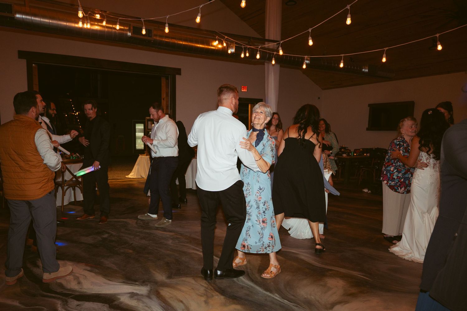 Wedding guests dancing together on a dimly lit dance floor with string lights overhead.
