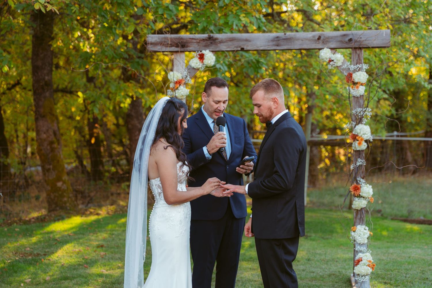 Outdoor wedding ceremony with decorated birch tree arch and autumn foliage.