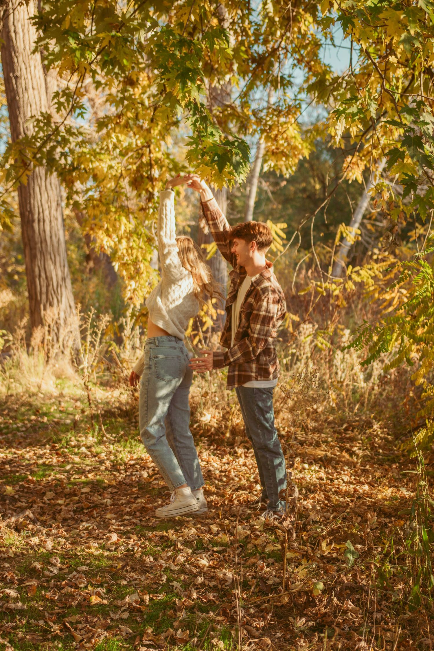 A couple dances playfully among fallen autumn leaves.