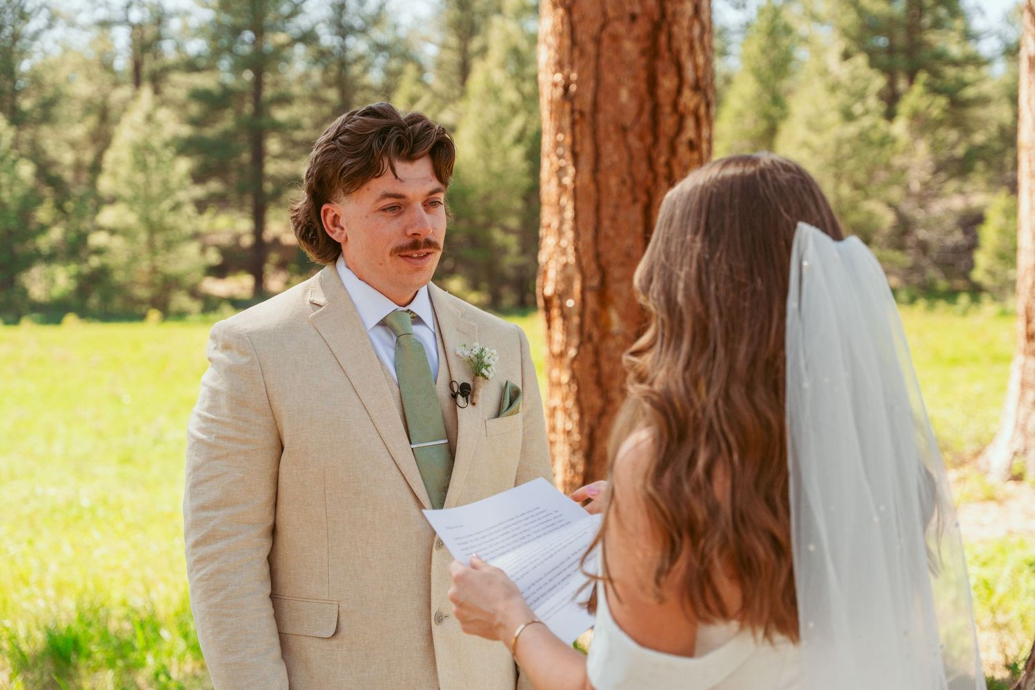 A couple shares an emotional first look moment in a sunlit forest setting.