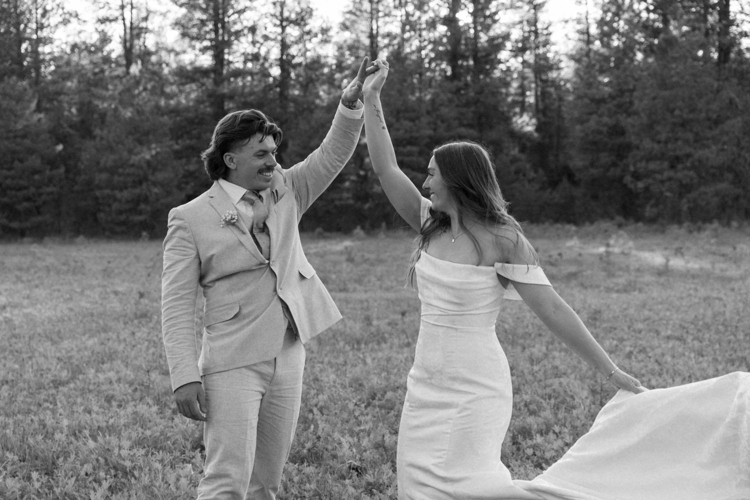 Black and white photo of a couple dancing joyfully in an outdoor setting.