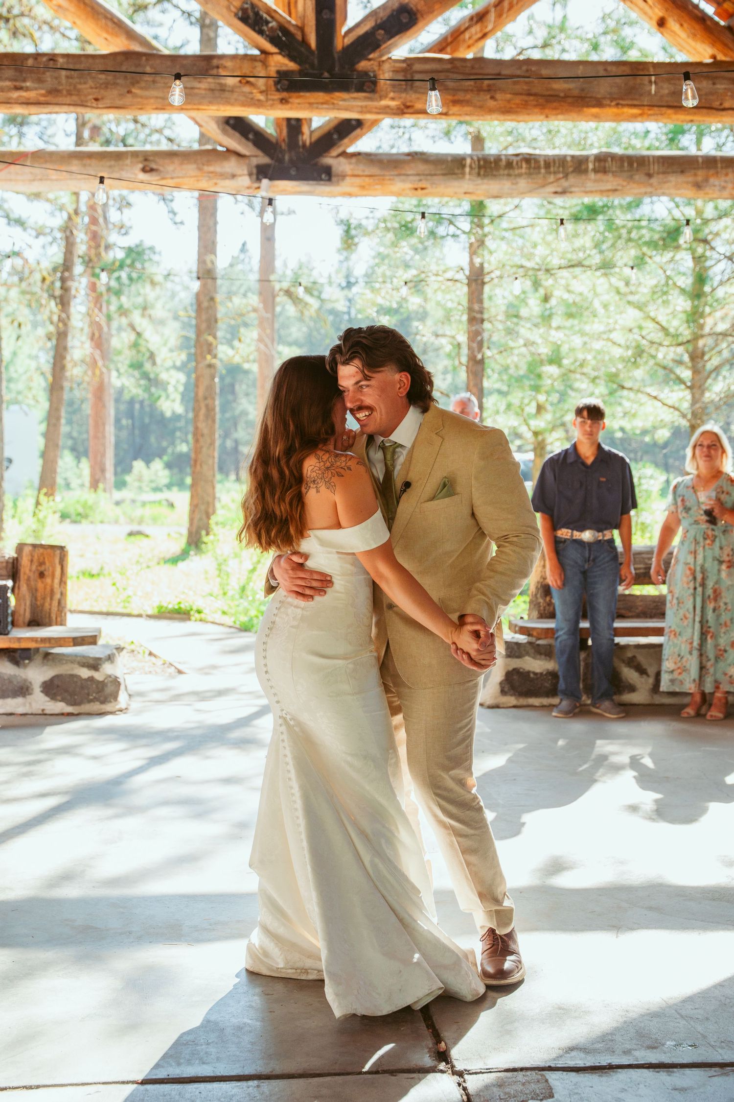 Newlyweds share their first dance in a rustic wooden pavilion surrounded by forest scenery.
