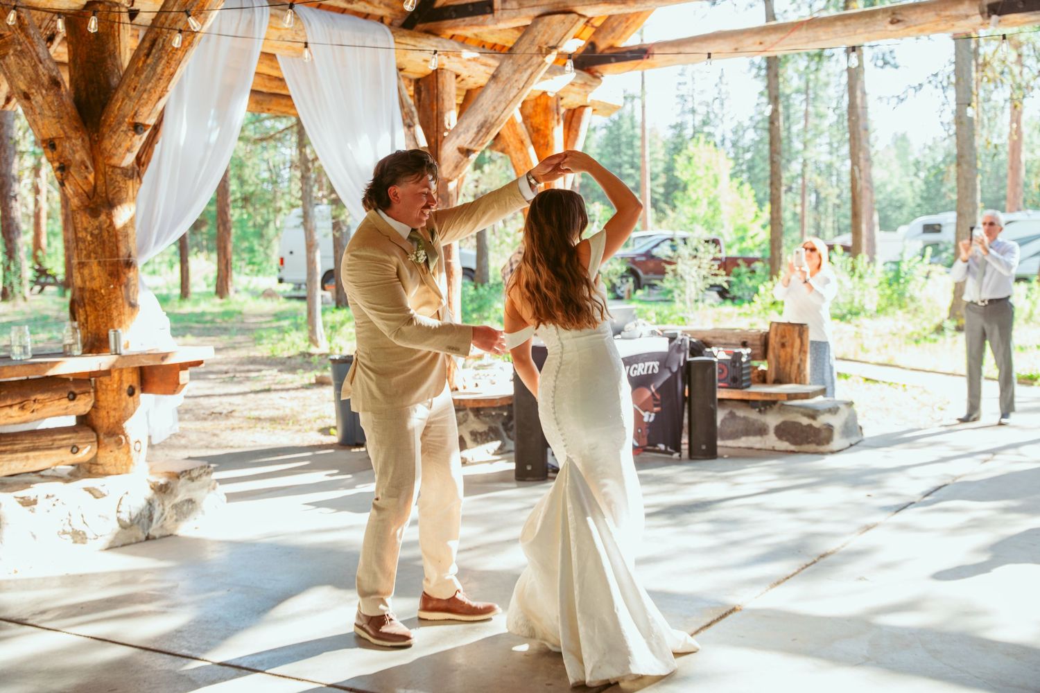 Newlyweds dance together under a rustic timber-frame structure with white flowing curtains.