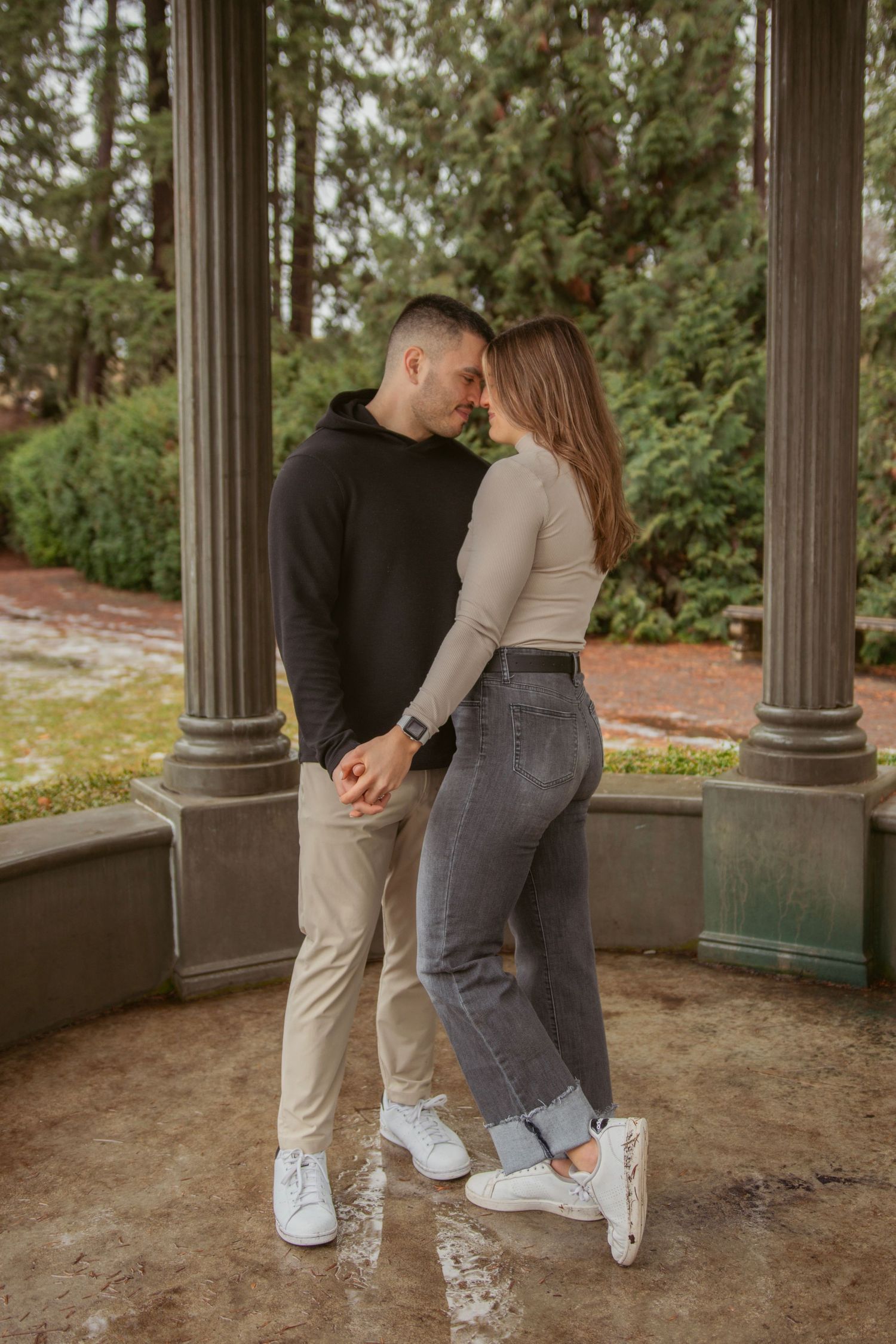 A couple shares an intimate moment under classical columns in a park setting.