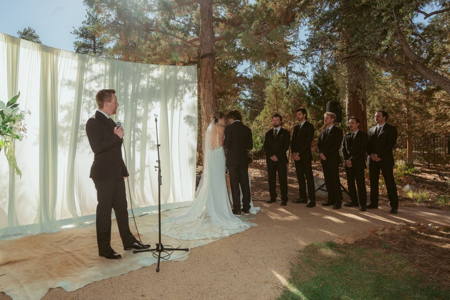 Outdoor wedding ceremony setup with white curtains and pine trees creating a natural forest backdrop.