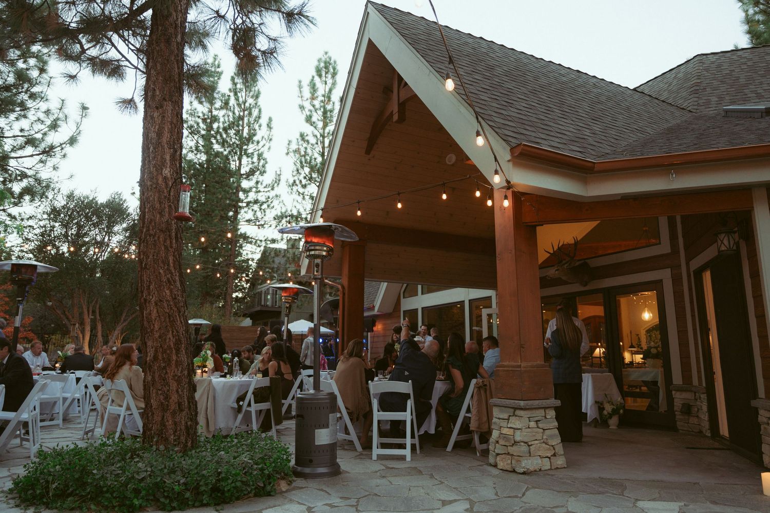 Rustic wedding venue exterior with string lights and wooden architecture at sunset.