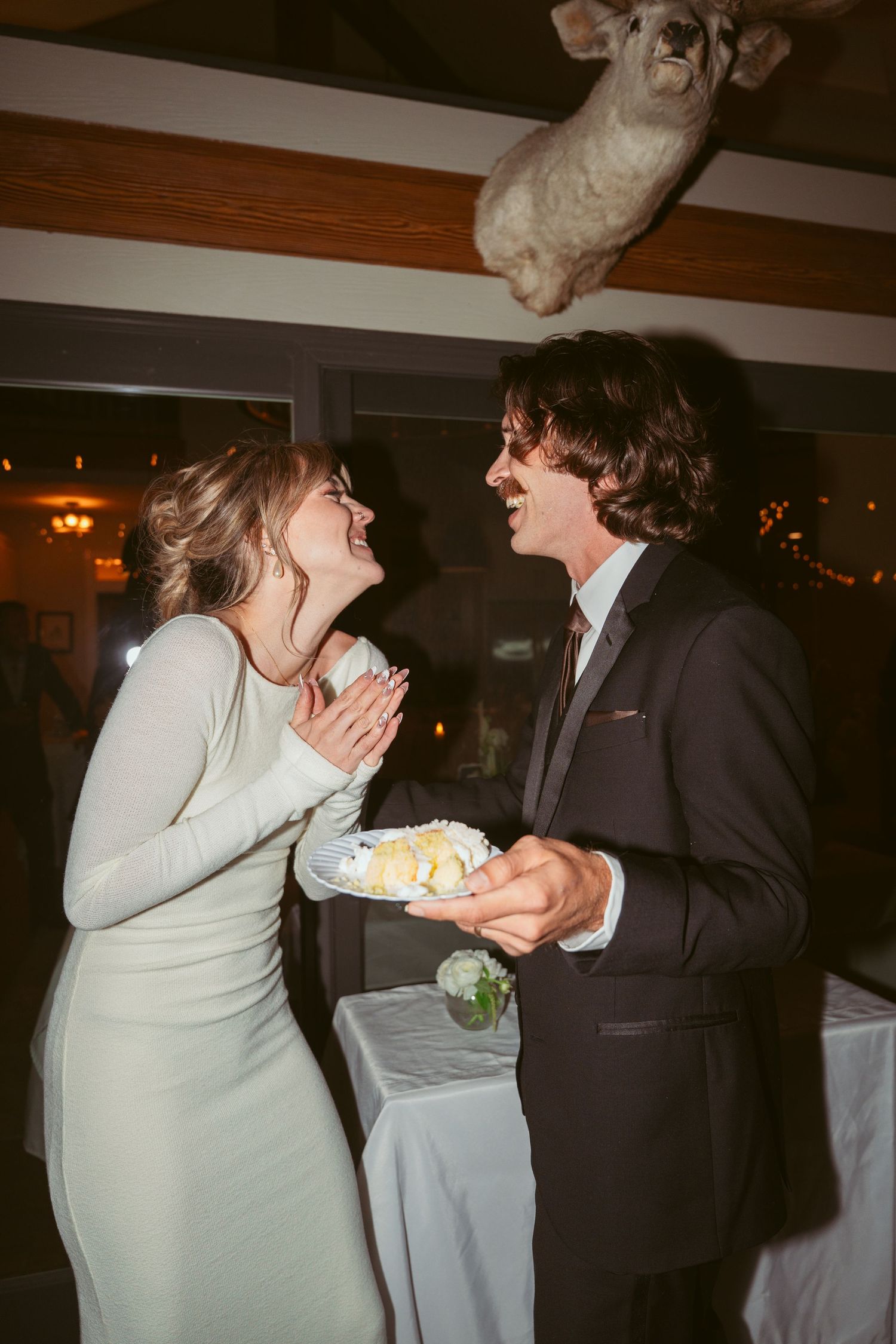 Wedding couple enjoys traditional cake cutting moment at indoor reception.