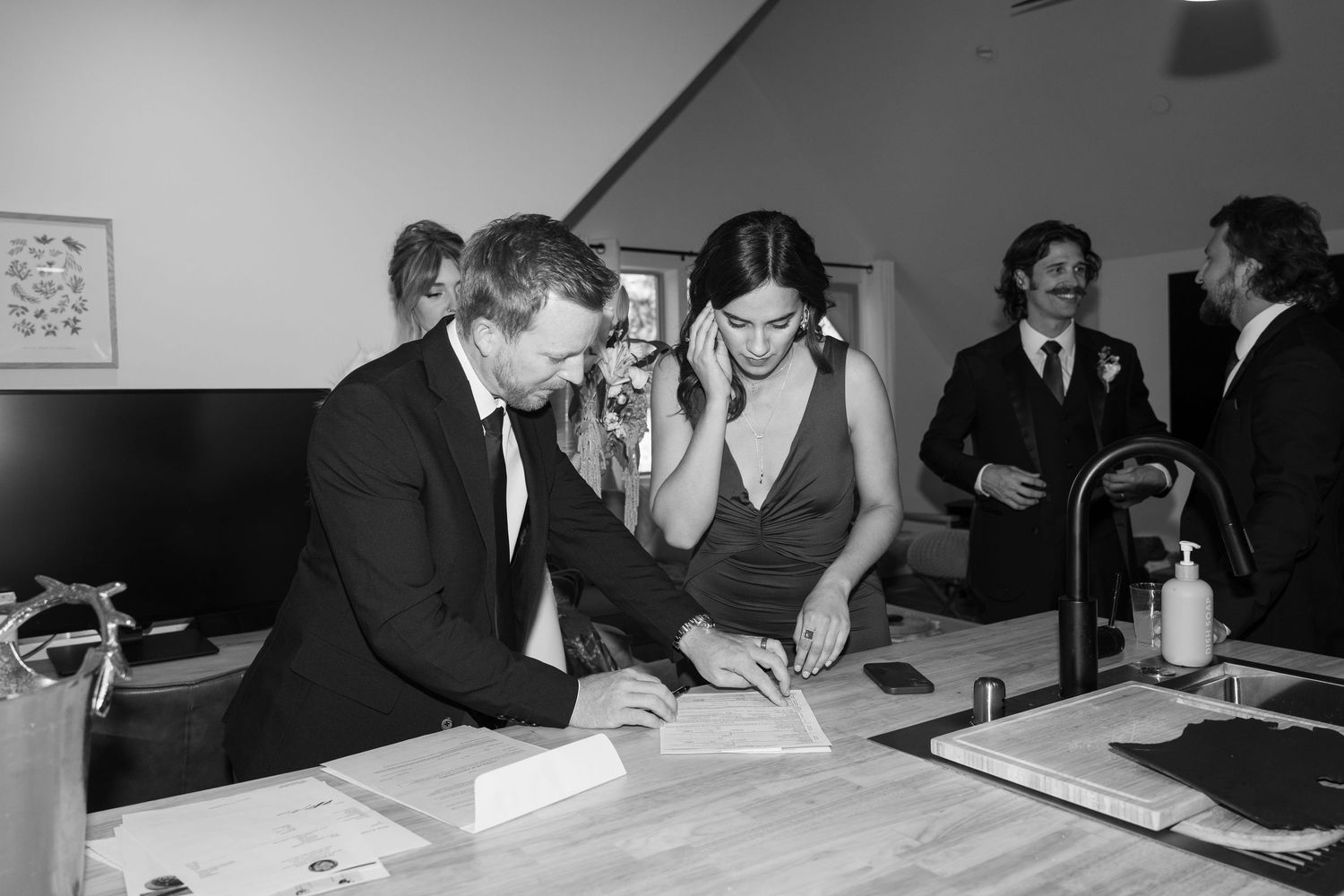 Wedding guests signing documents at a table during an indoor ceremony.