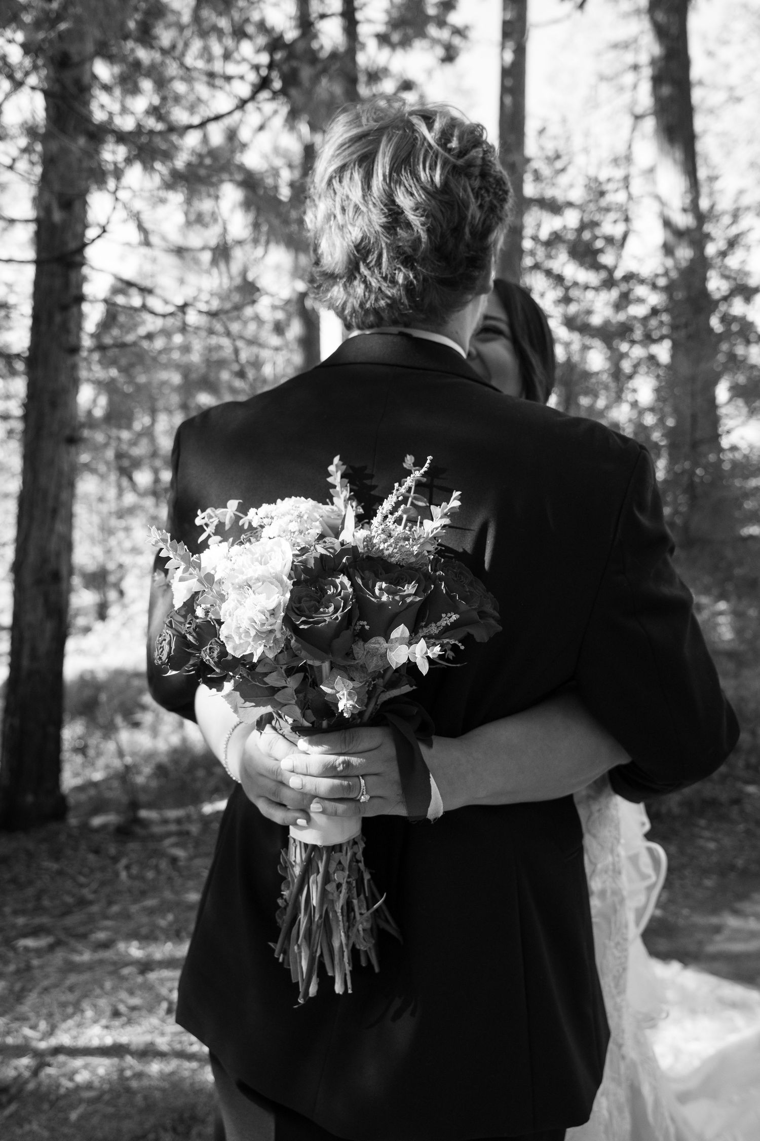 A black and white photo of a couple embracing with a wedding bouquet behind the groom's back.