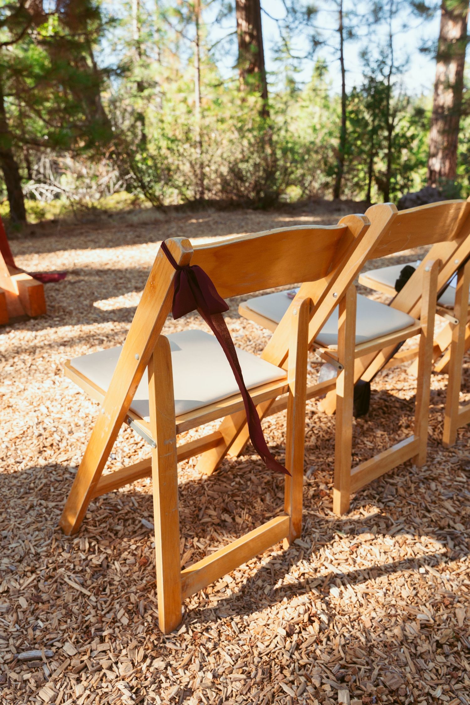 Wooden folding chairs lined up outdoors on wood chips for a garden wedding ceremony.