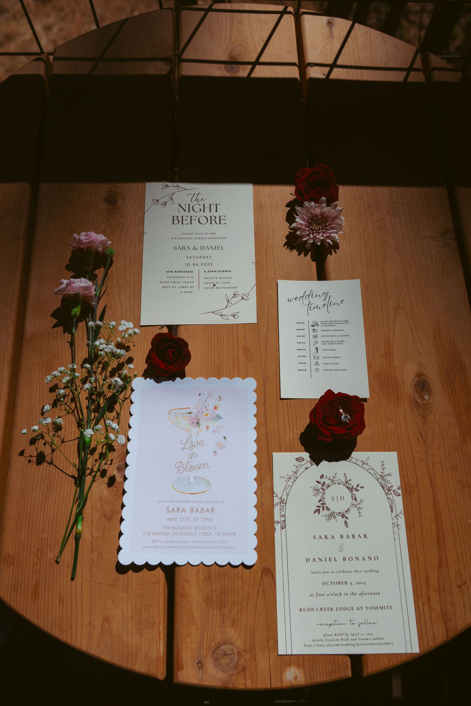Wedding stationery and dark red flowers arranged artistically on wooden surface.