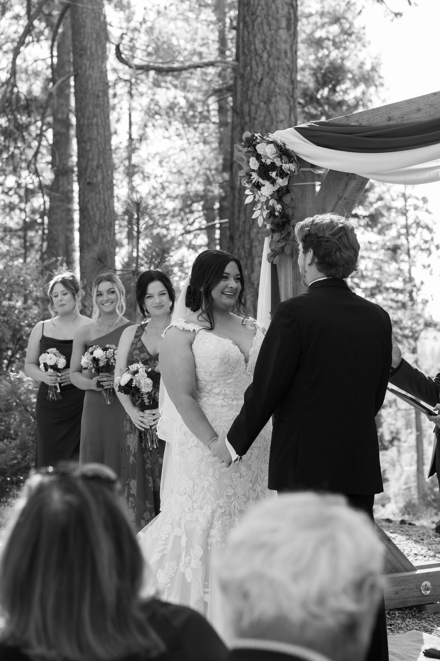Wedding ceremony taking place under tall pine trees with guests watching.