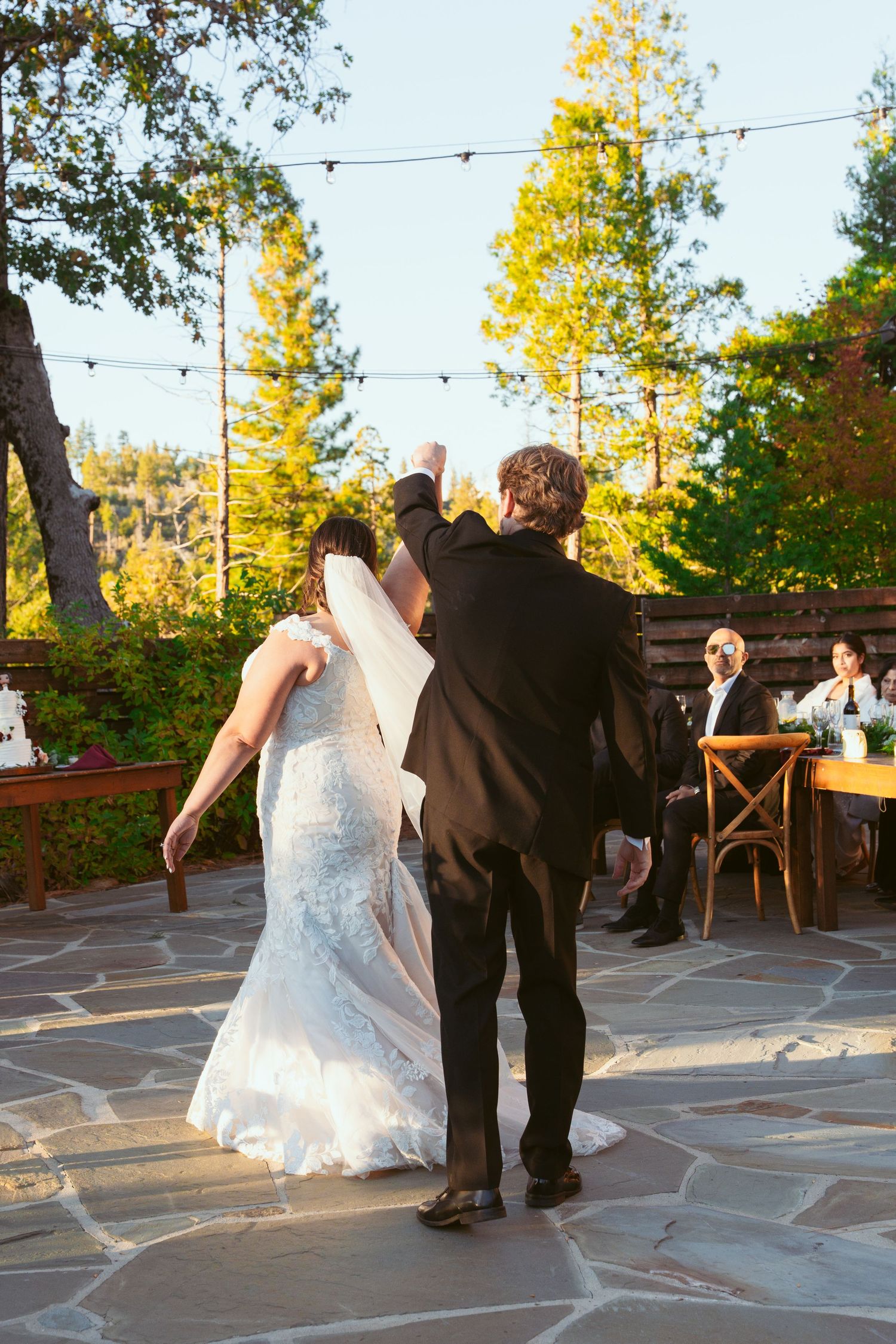 Couple dancing together on a stone patio with string lights and autumn trees in the background.