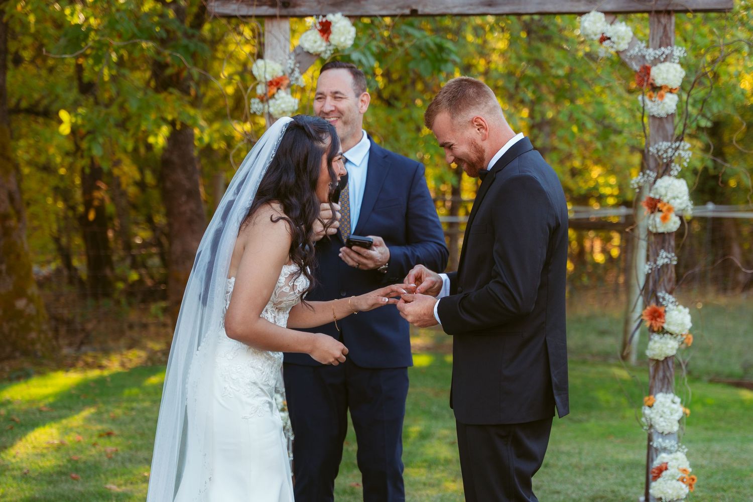 Wedding ceremony under decorated arch with autumn foliage in background.