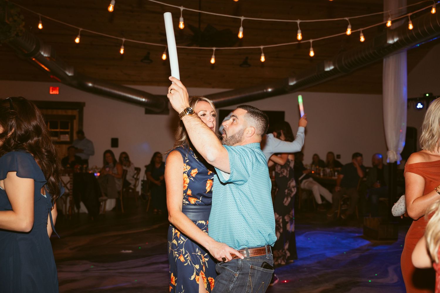 Wedding guests dancing and celebrating on a spacious dance floor with string lights overhead.