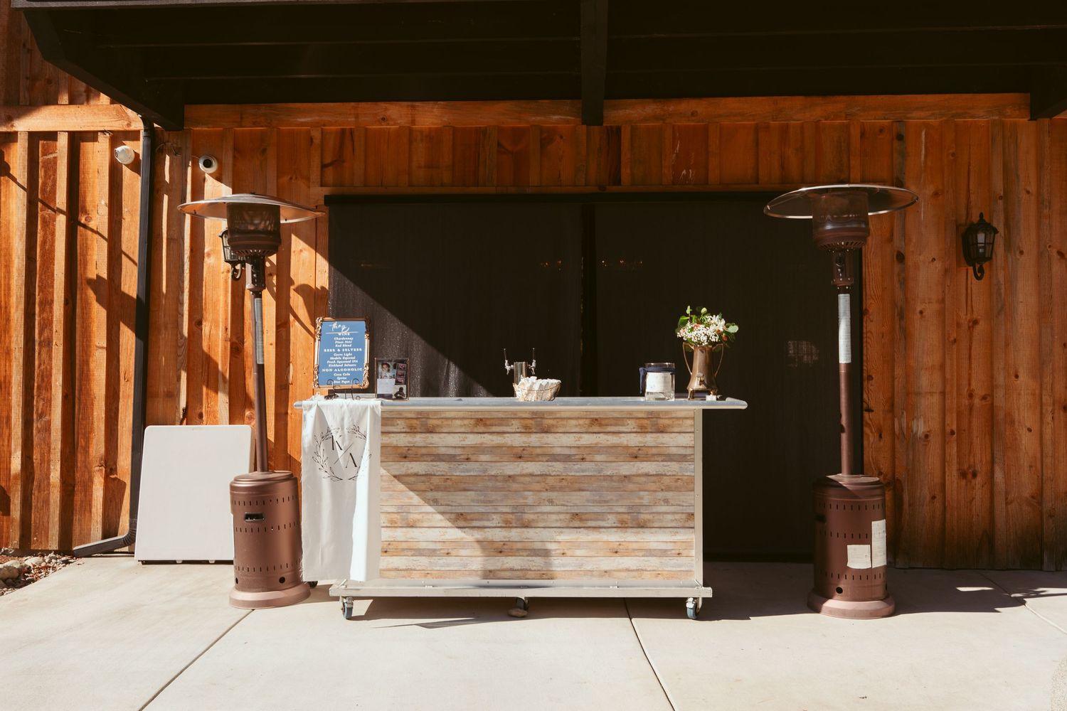 Rustic wooden bar setup at barn wedding venue with heaters and minimal decor.