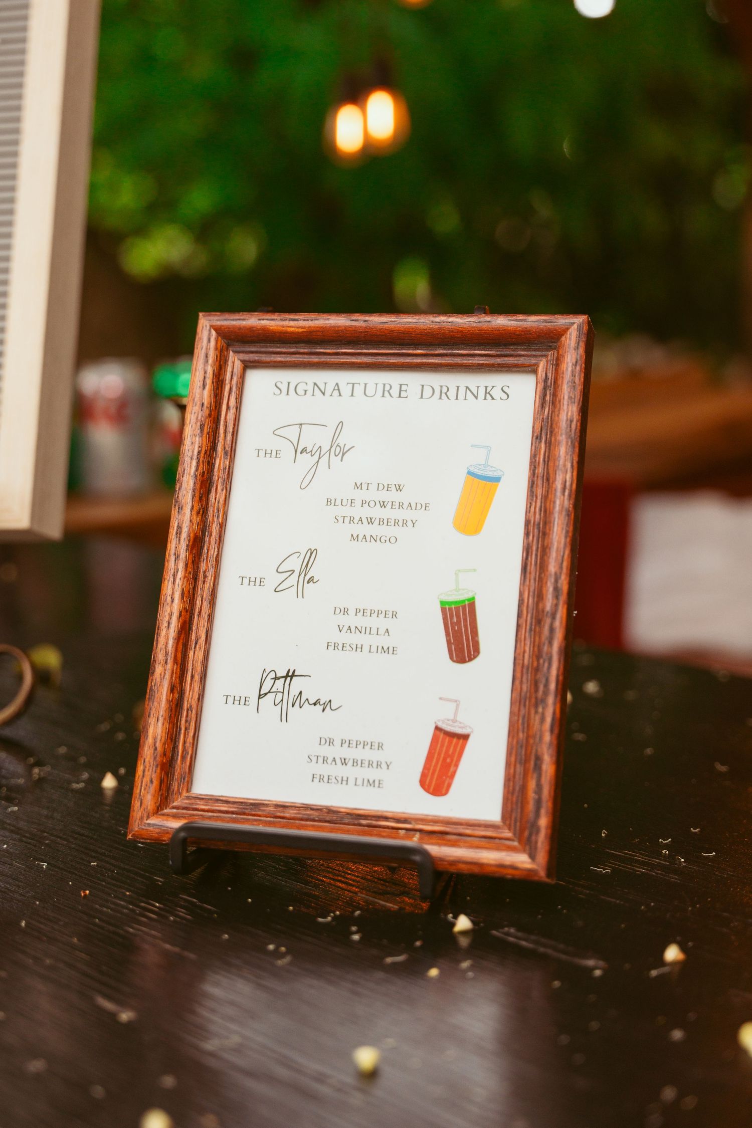 Framed signature drinks menu displayed on dark table at wedding reception.