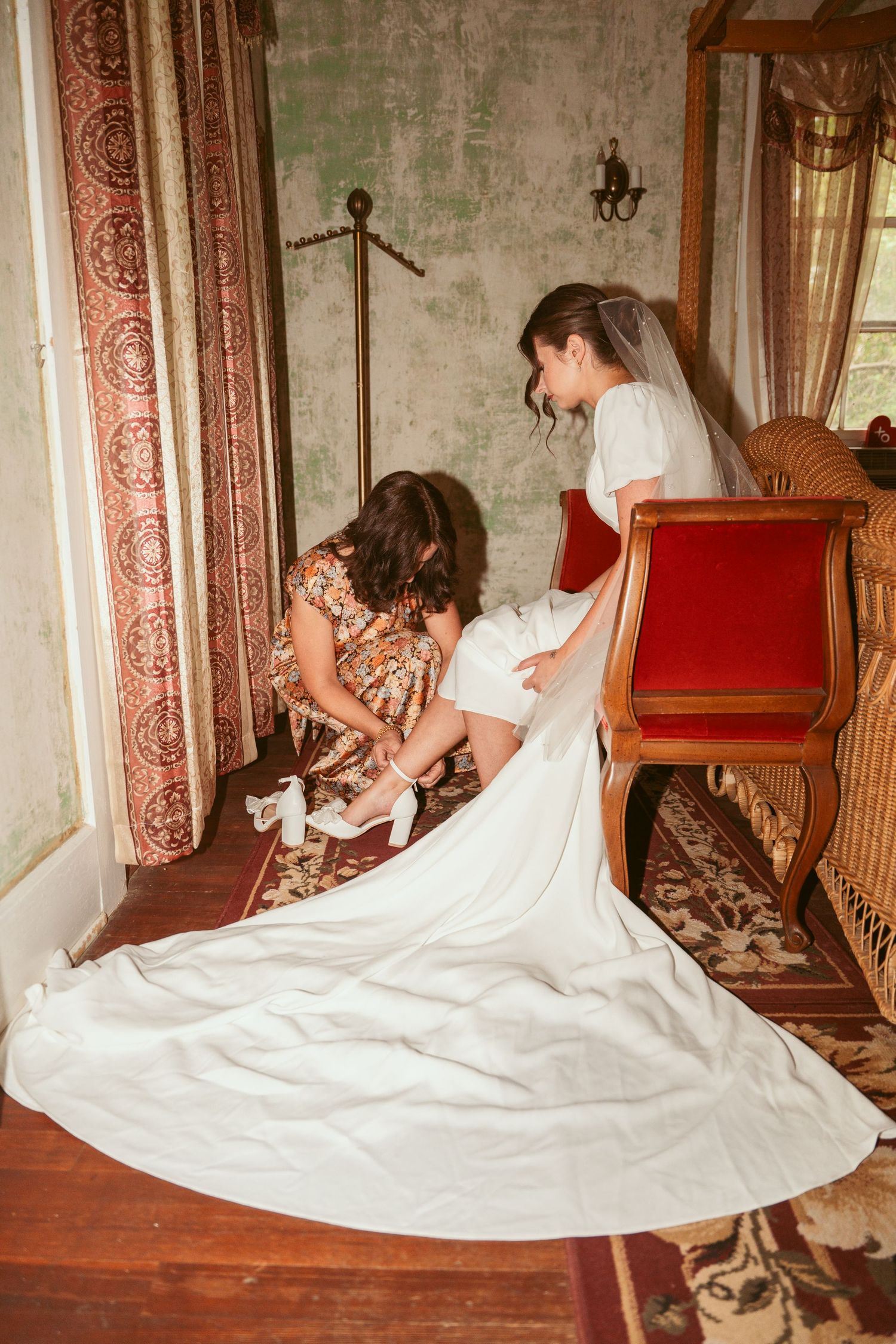 Helping with bridal shoes on vintage wooden stairs with elegant dress train flowing down.