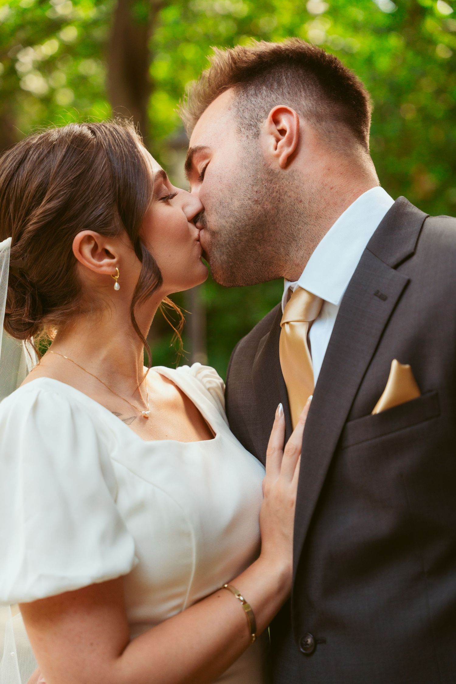Romantic wedding kiss captured in natural outdoor setting with soft green background.
