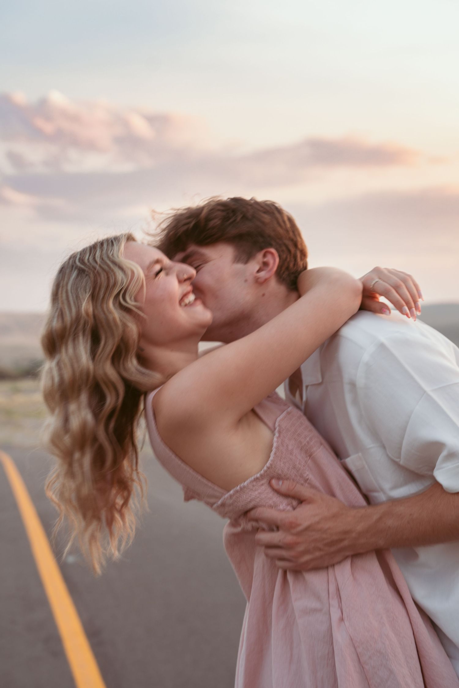 A couple shares a tender moment on a desert road during golden hour.