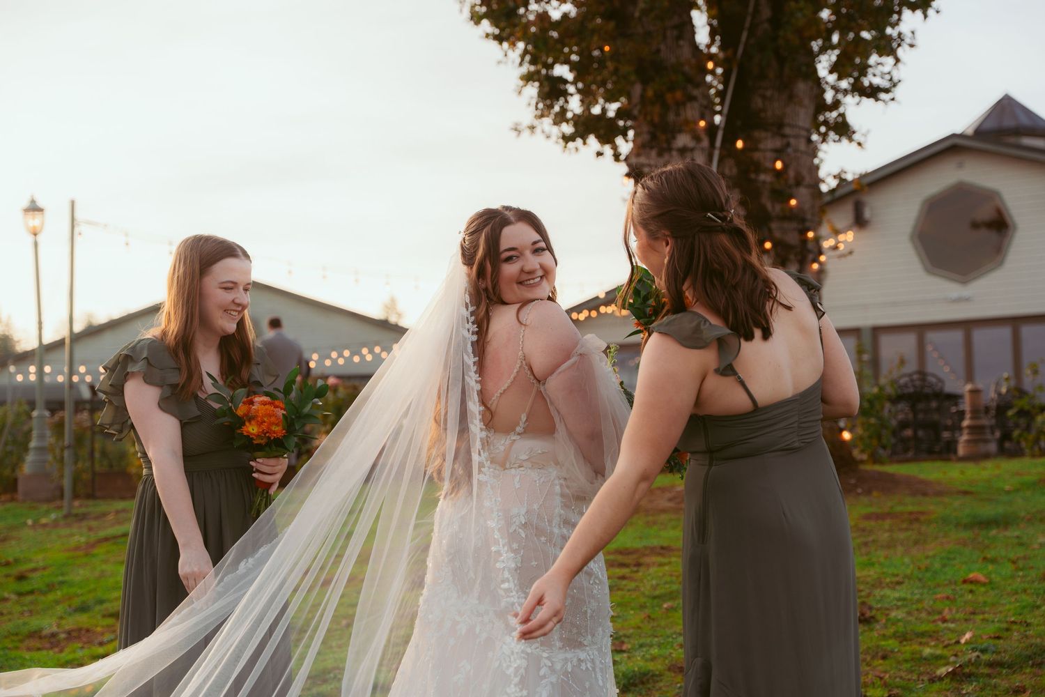 Wedding party helps adjust bride's flowing veil during outdoor autumn photoshoot.