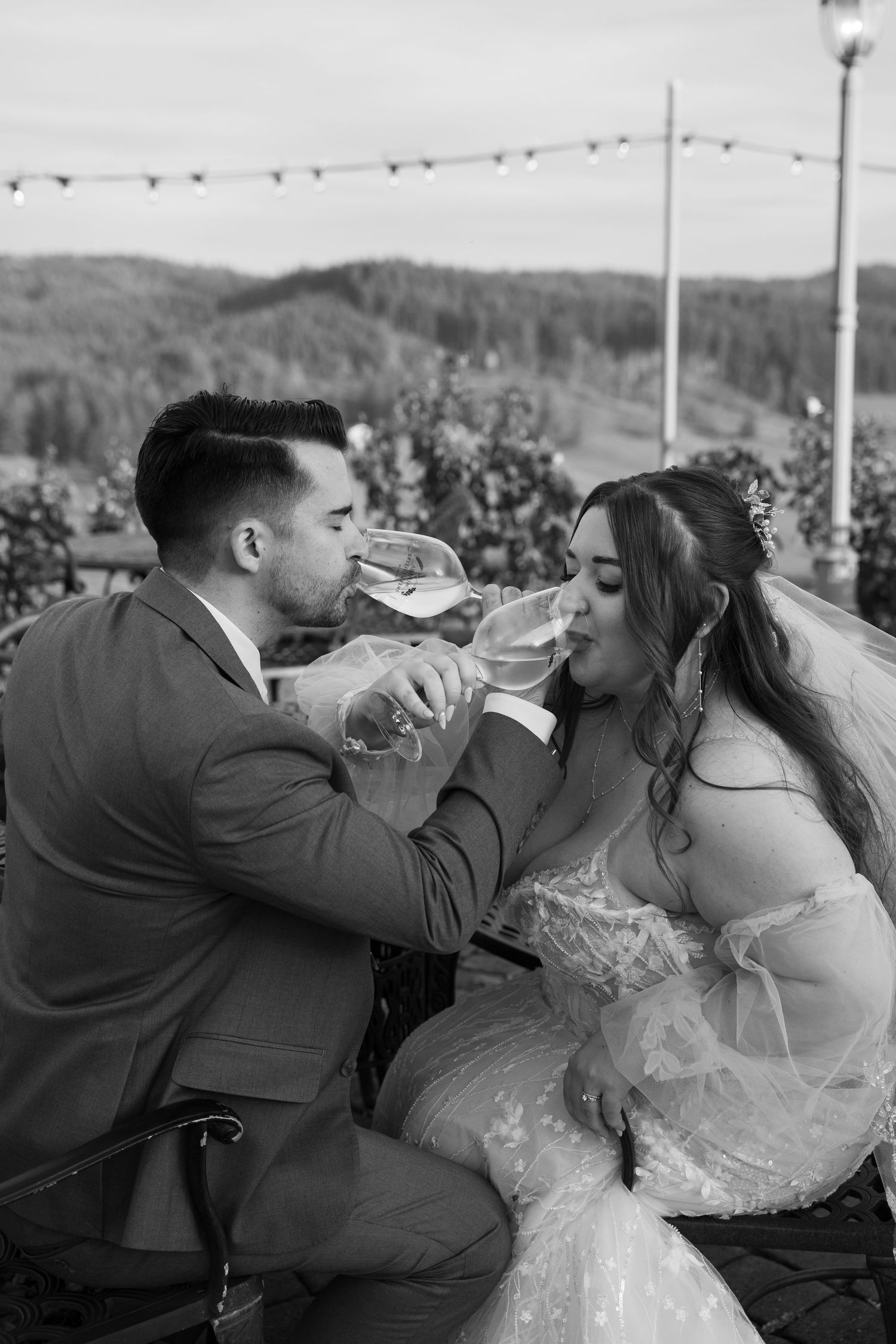 Black and white photo of newlyweds drinking wine together at vineyard celebration.