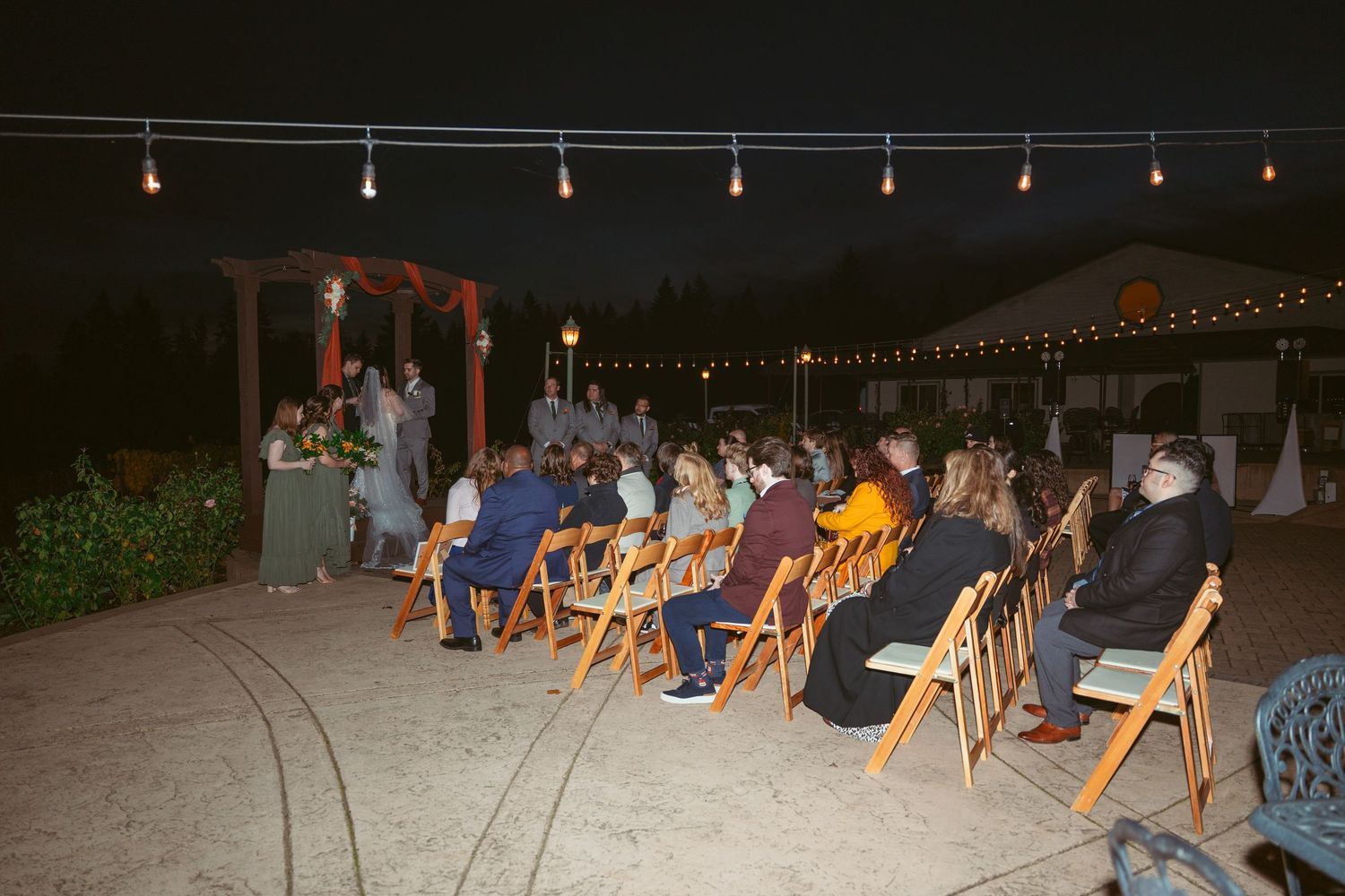 String lights create a romantic ambiance over outdoor wedding reception seating area.