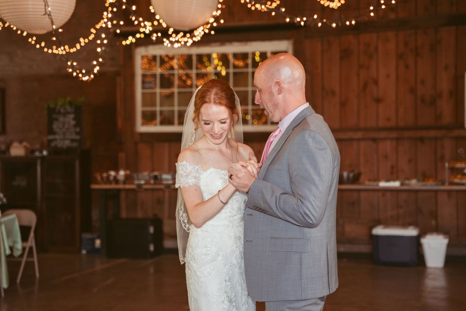 Special dance moment in rustic barn reception with warm lighting and paper lantern decorations.