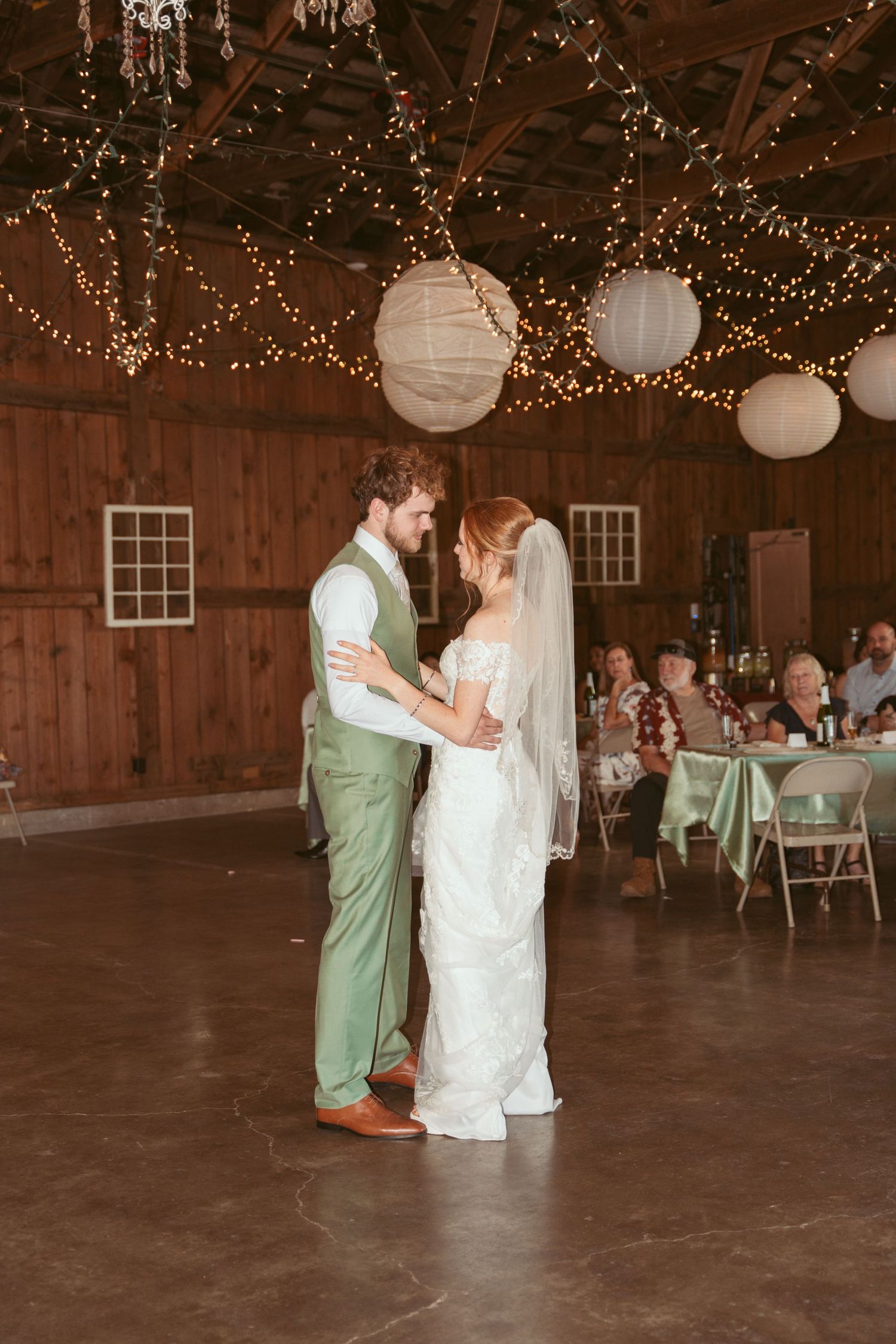 Wedding dance in a rustic barn venue illuminated by string lights and paper lanterns.