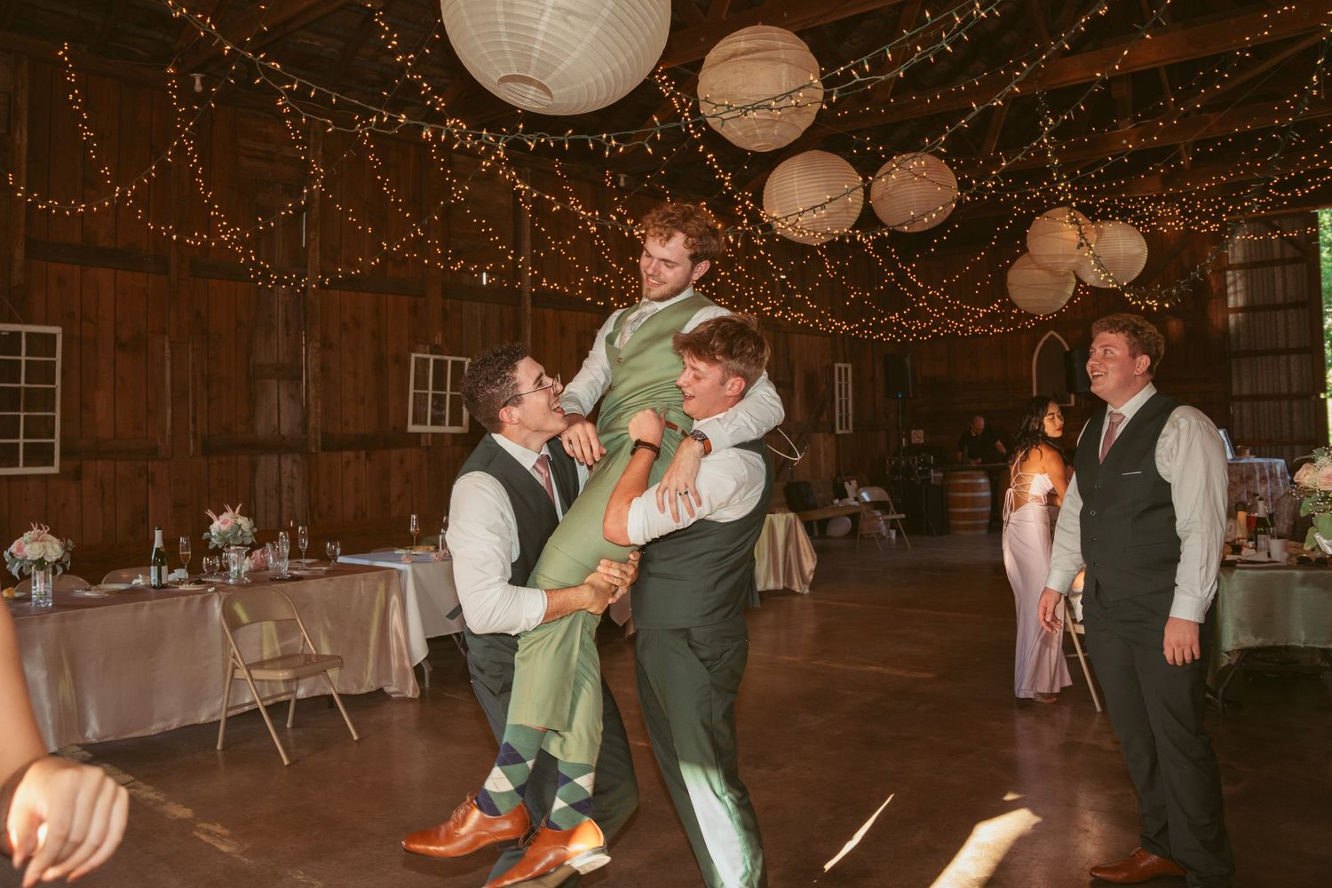Lively dance sequence at a barn wedding with fairy lights and paper lanterns overhead.