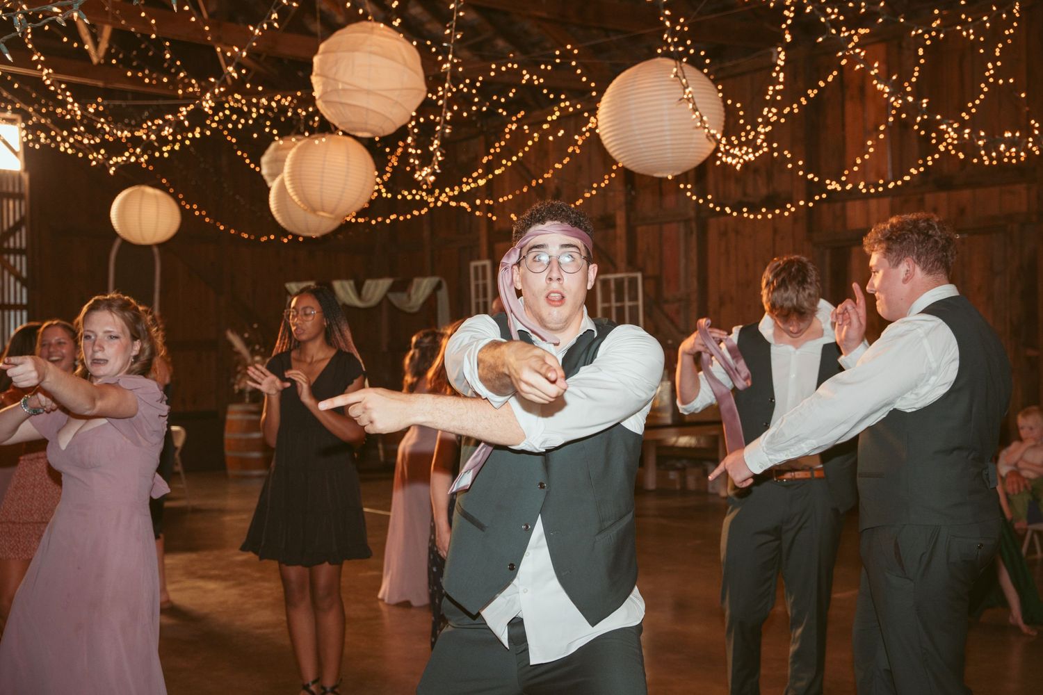 Wedding guests dancing under string lights and paper lanterns at an indoor reception venue.